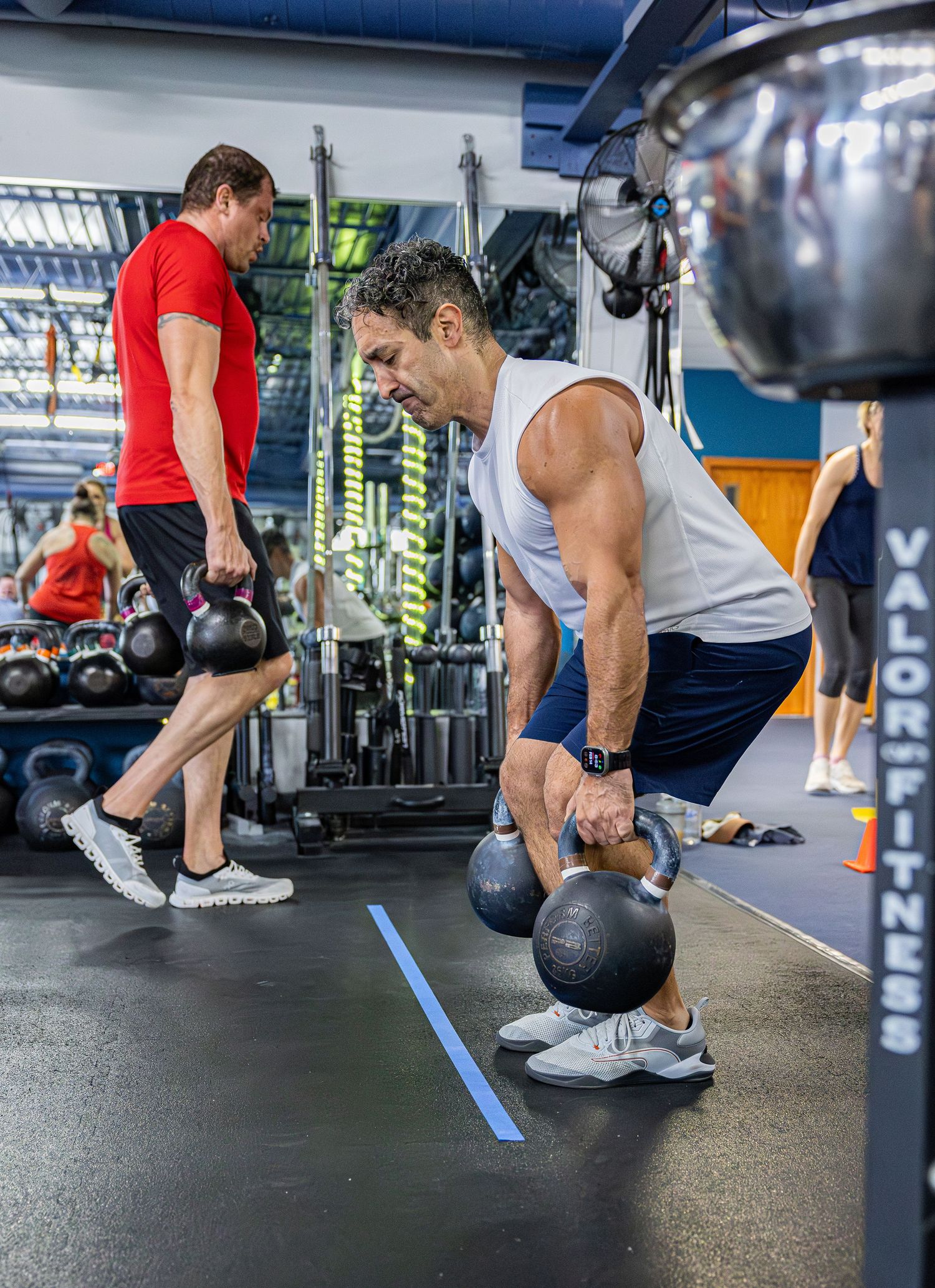Two men performing kettlebell exercises at Valor Fitness gym during a workout.