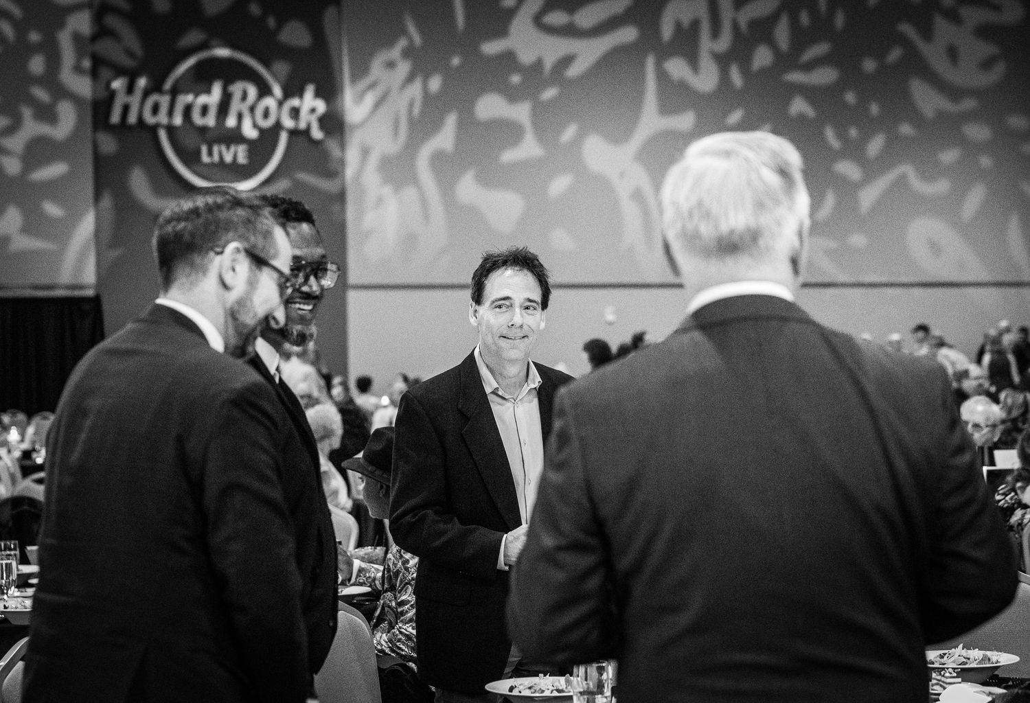 Men in business attire converse at a Hard Rock Live venue during a networking event.
