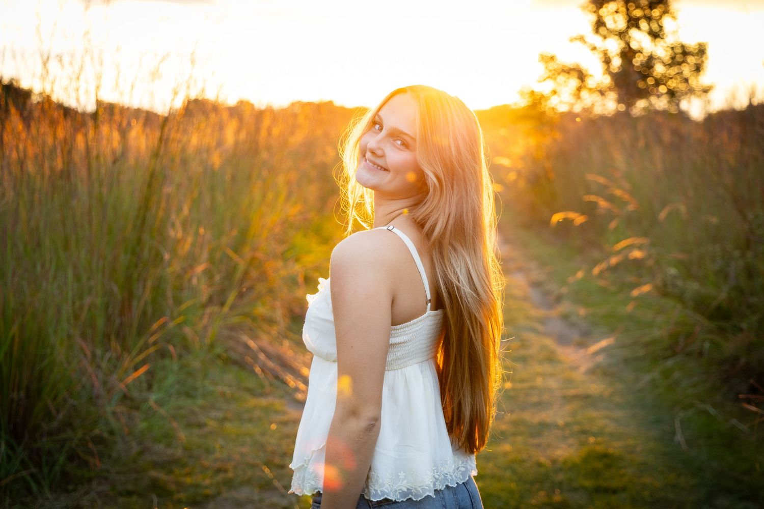 Young blonde girl smiling over her shoulder in a sunlit field during golden hour sunset.