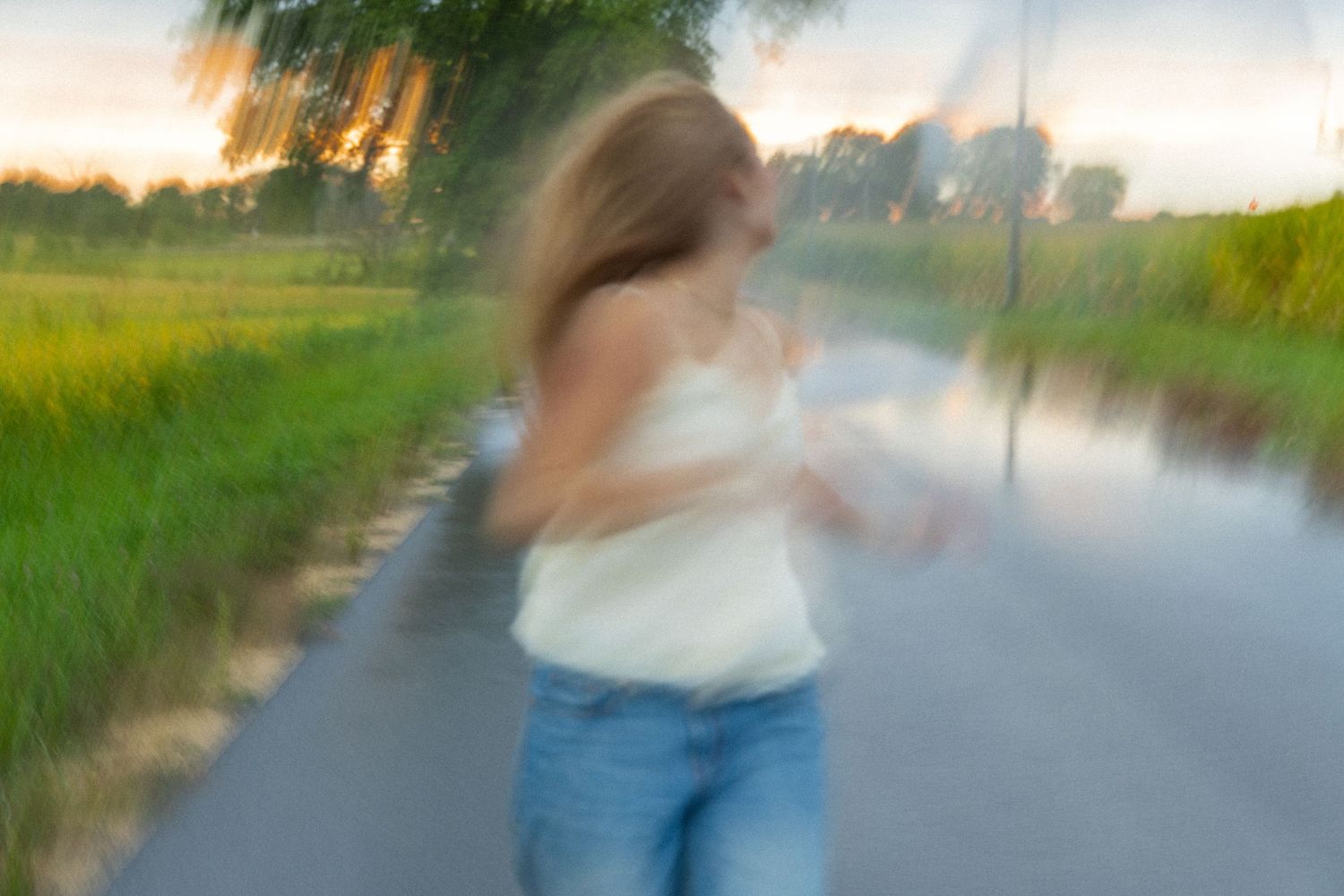 Blonde girl in white top and jeans running along scenic rural road at dusk.