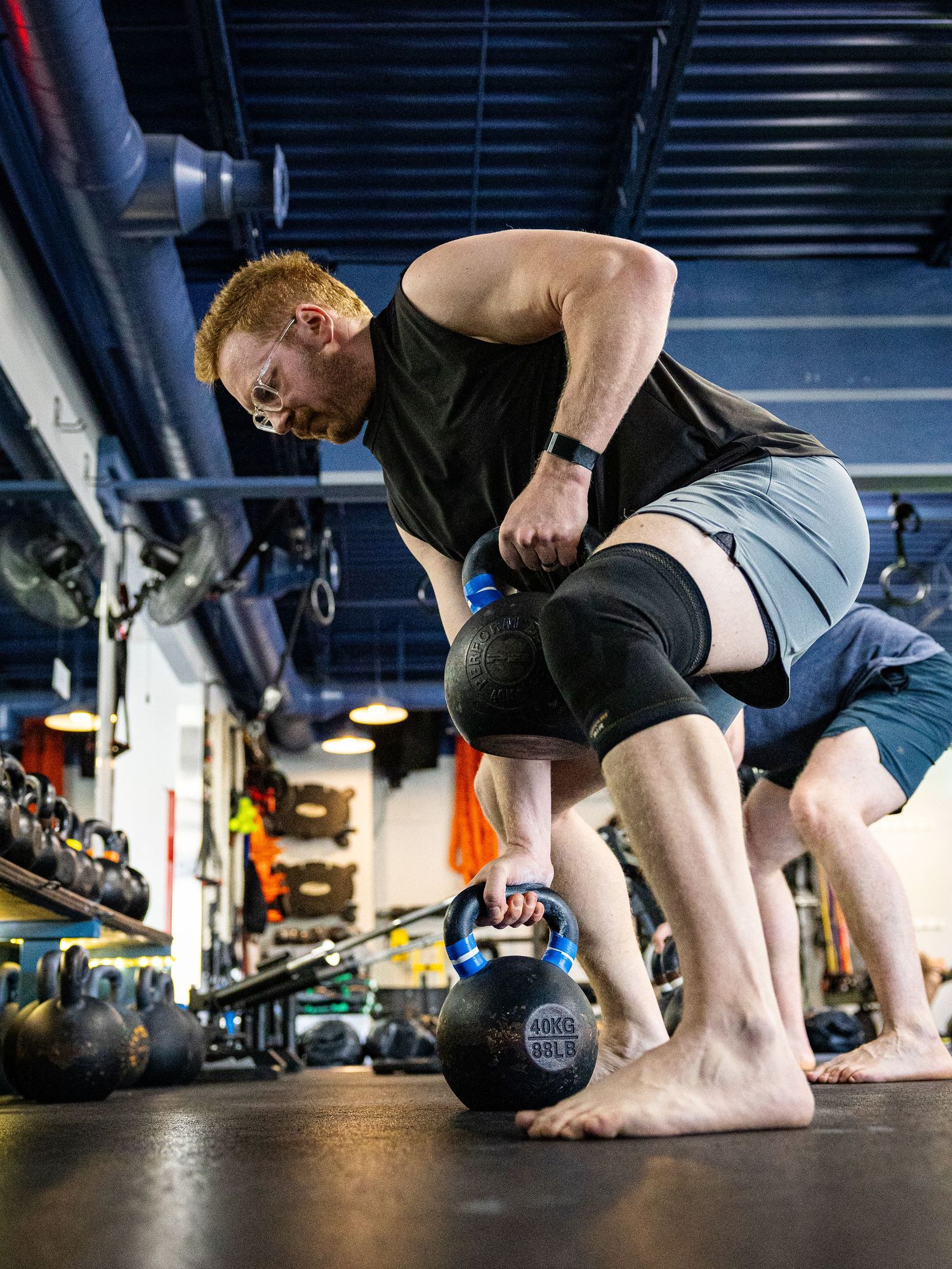 Muscular redhead man lifting a kettlebell barefoot during a gym training session.