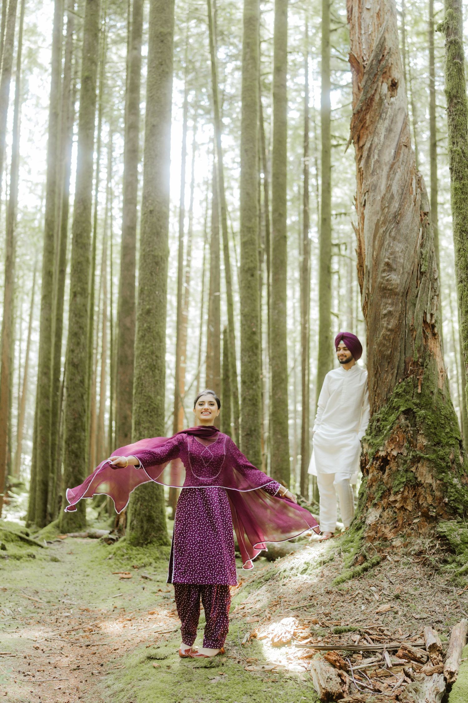 Sikh couple in traditional attire posing in a sunlit forest with tall trees.