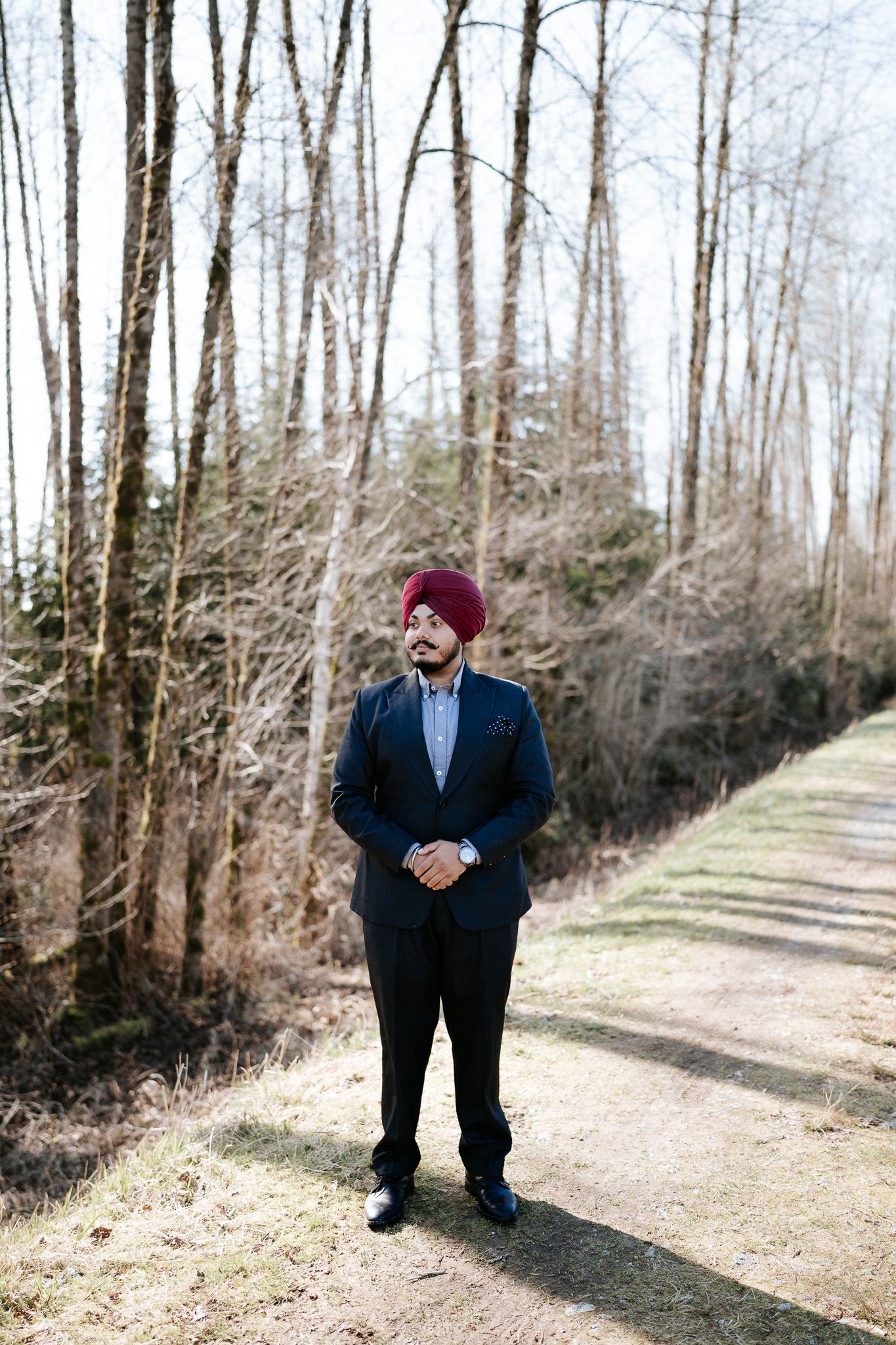 A person wearing a red beanie and navy suit stands on a wooded path during winter.