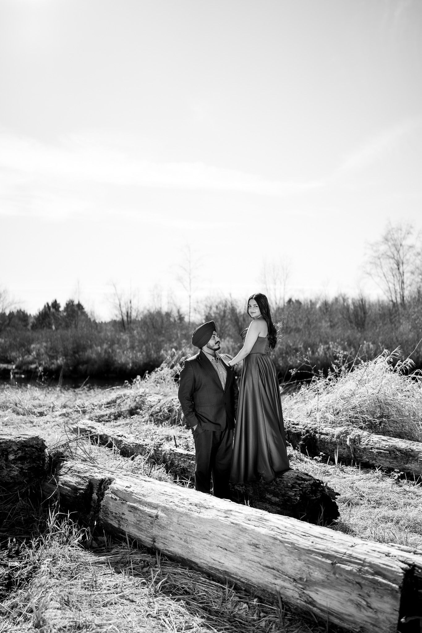 Two figures in dark cloaks sit on a fallen log in a snowy winter landscape.