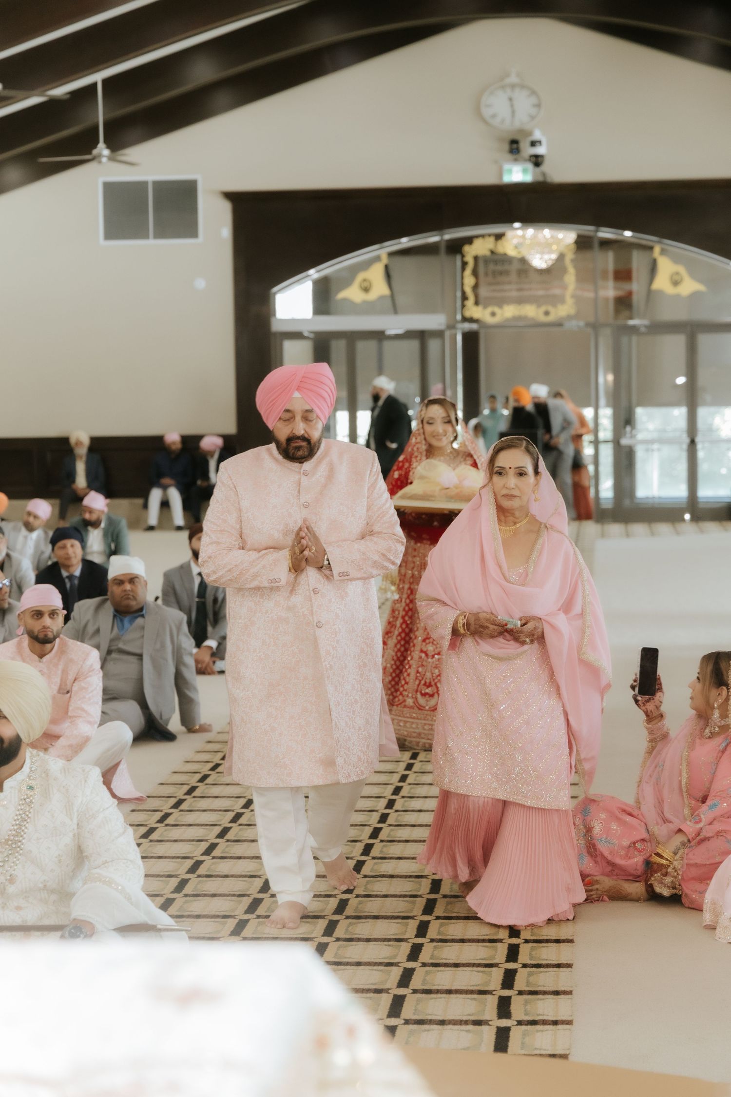 Sikh couple in pink attire walking during a traditional Anand Karaj wedding ceremony in a Gurdwara.