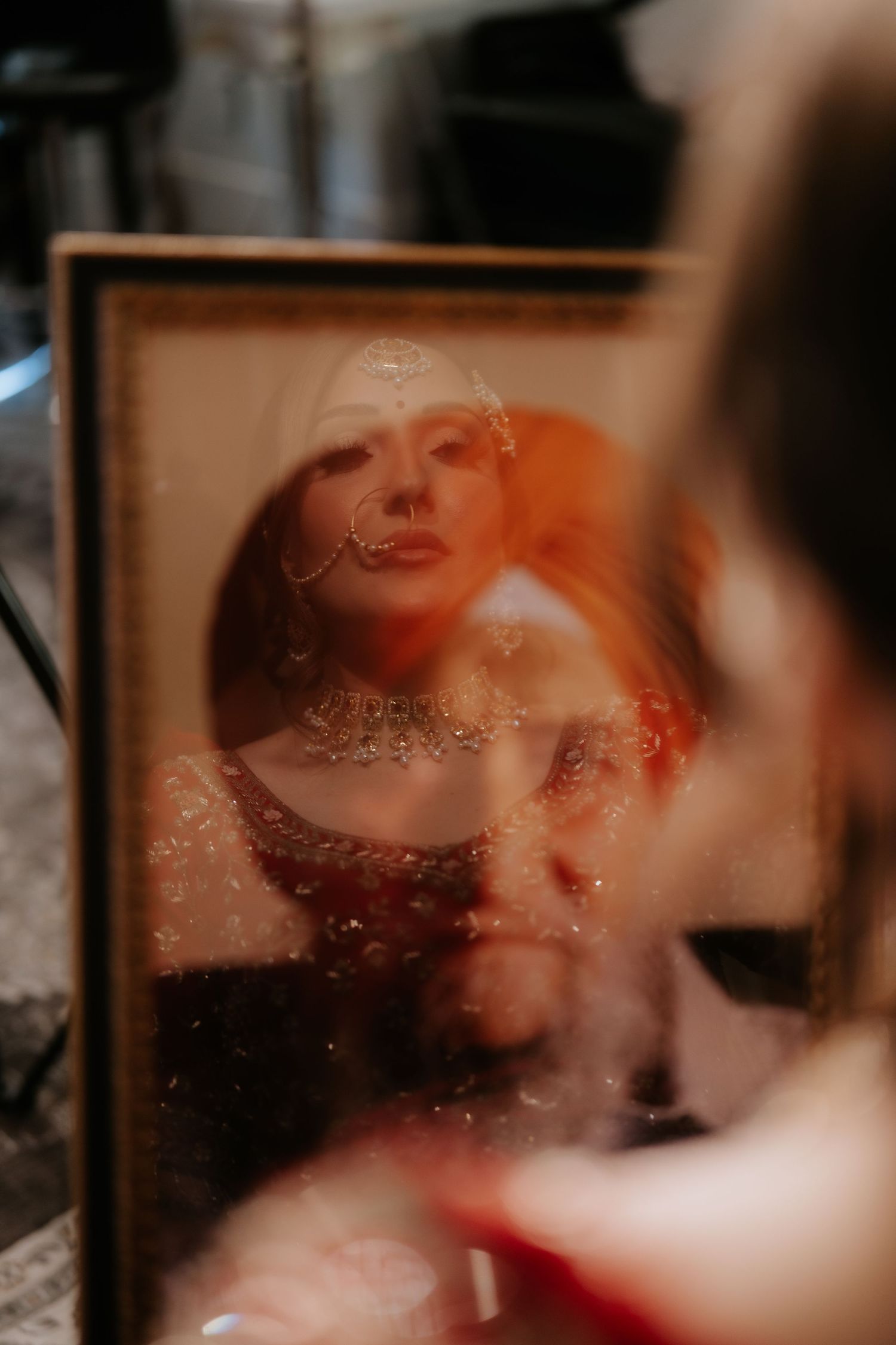Woman in red dress with silver necklace and hoop earrings reflected in an ornate vintage mirror.