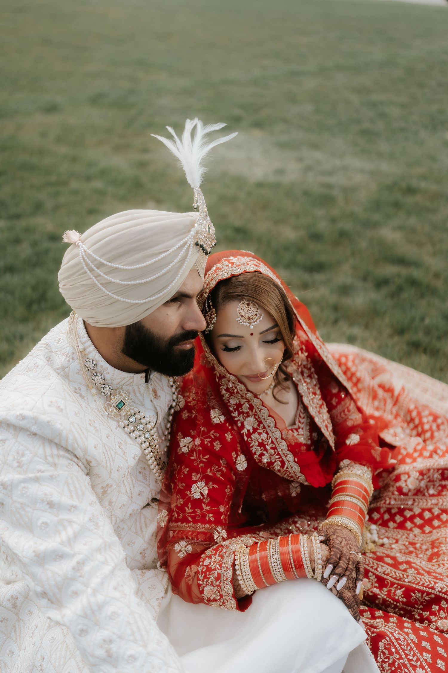 Sikh bride in red lehenga and groom in white sherwani and turban share an intimate moment at their wedding.
