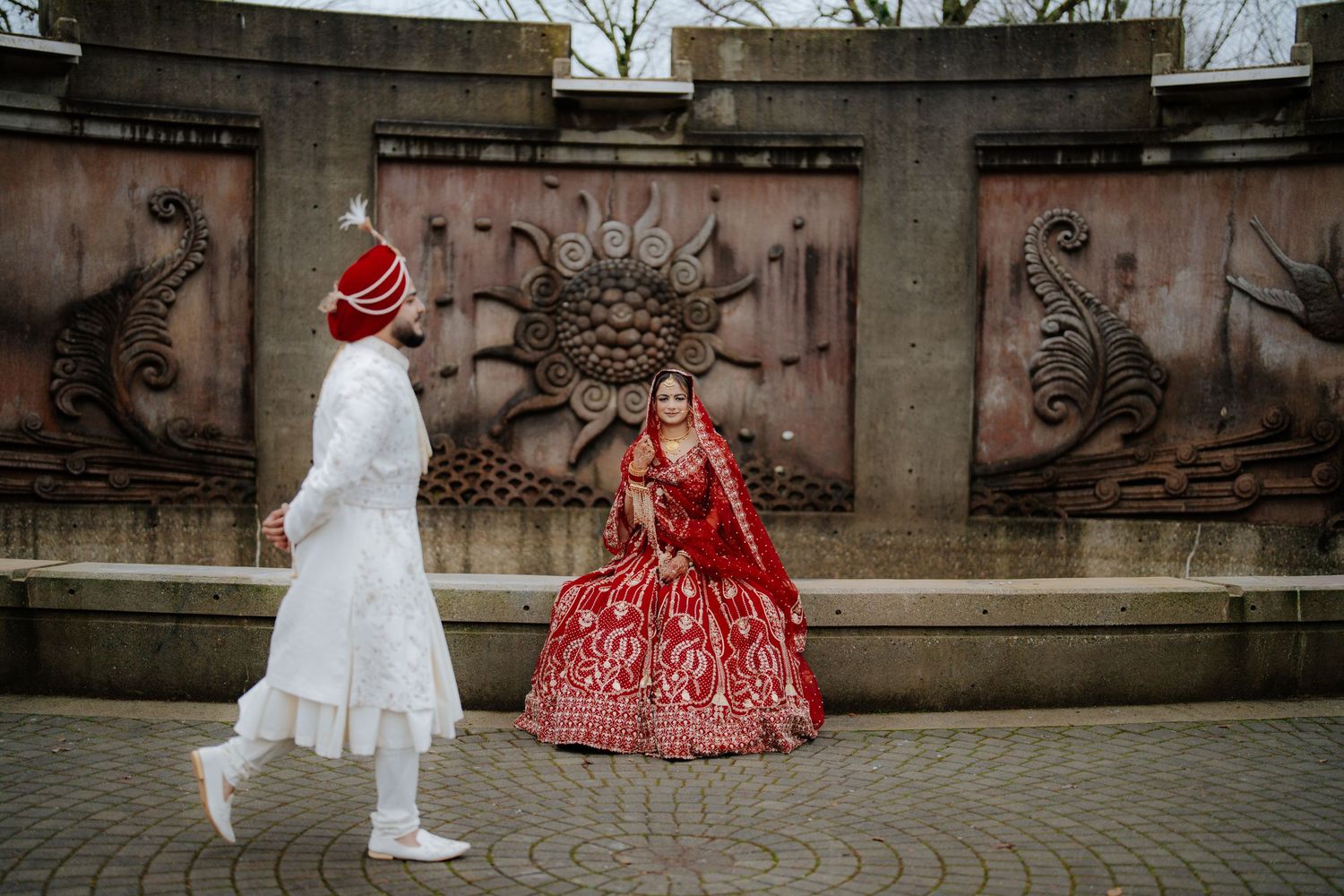 Elegant wedding couple in traditional Indian attire photographed against stone columns.