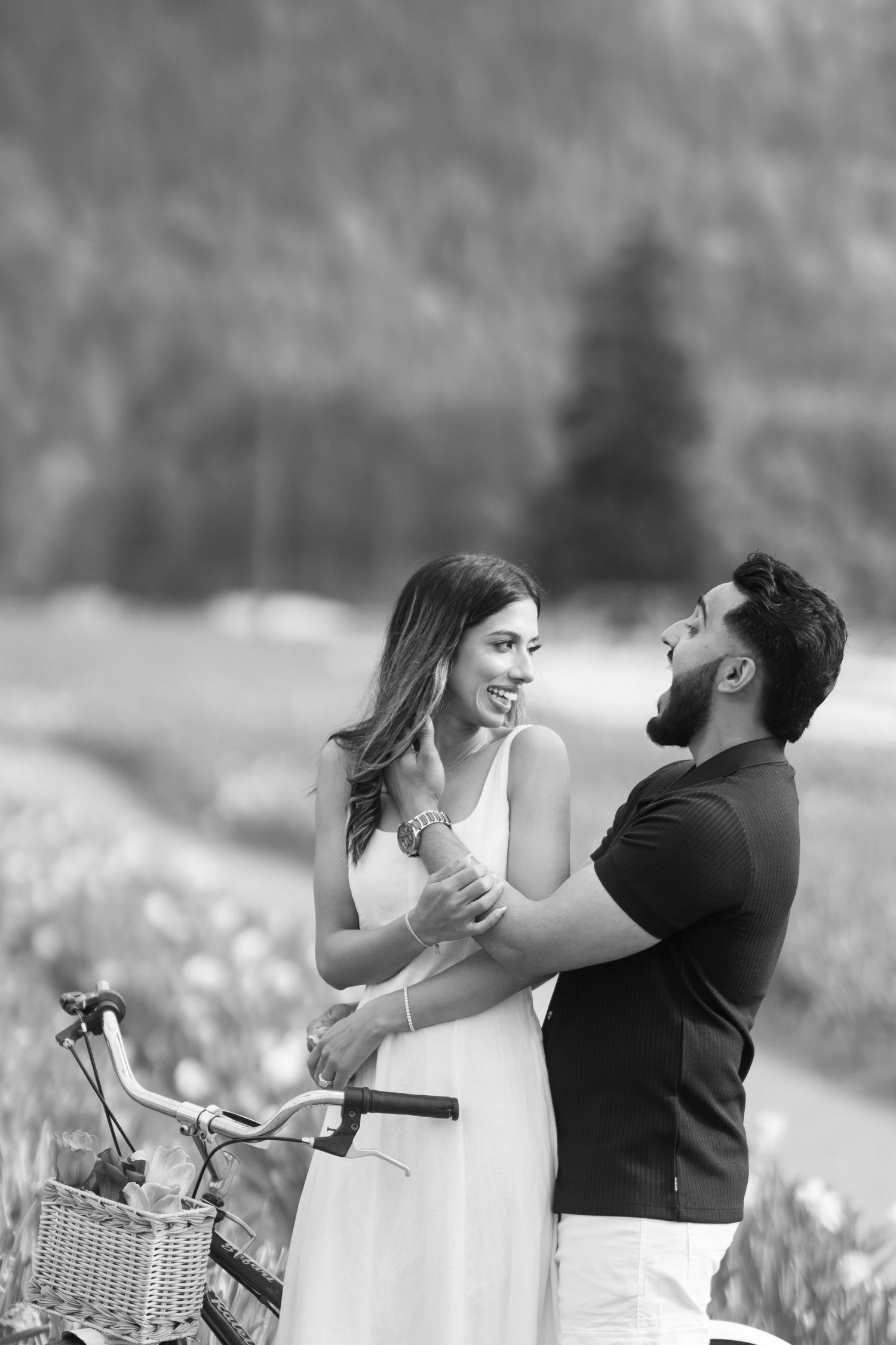 A romantic black and white photo sequence of a couple laughing and embracing near a bicycle with a basket.