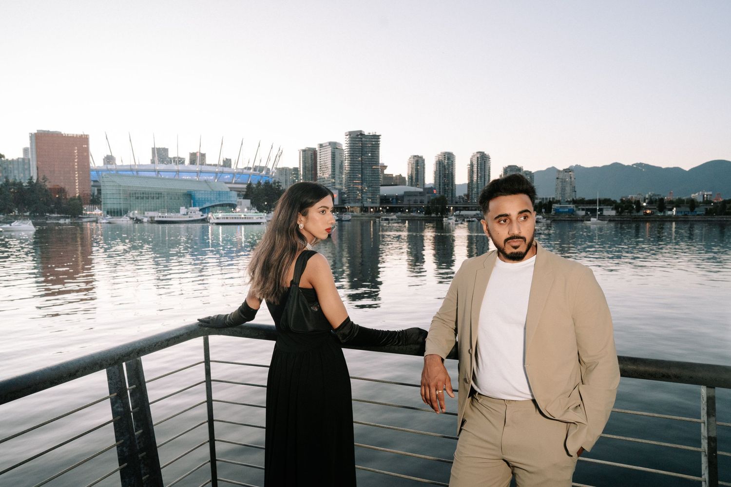 A couple enjoys a romantic moment on a waterfront deck with city skyline views during sunset.