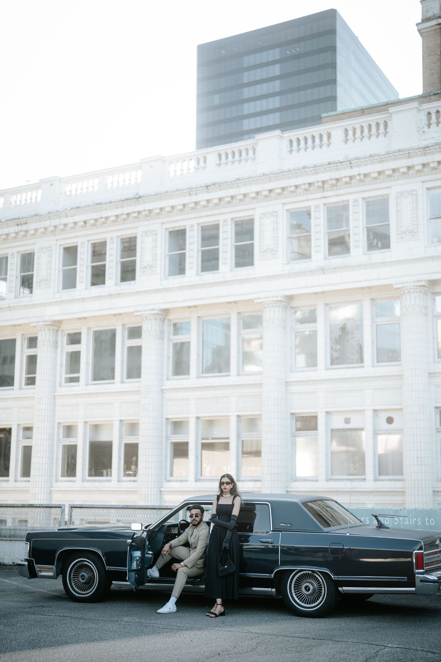A vintage black Lincoln Continental luxury car parked in front of a white commercial building with modern architecture.