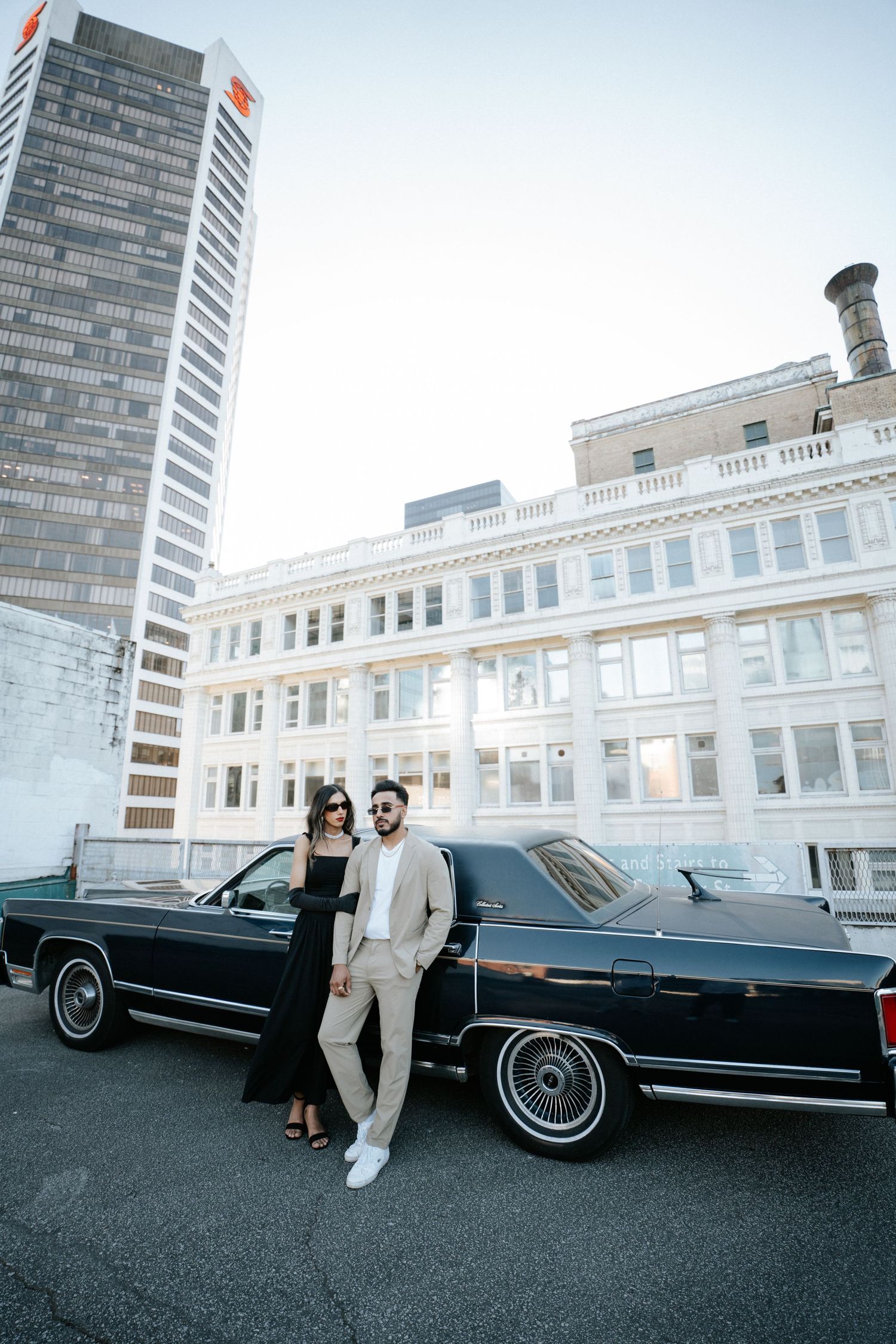 A classic black vintage car parked in front of a white building with people standing beside it.