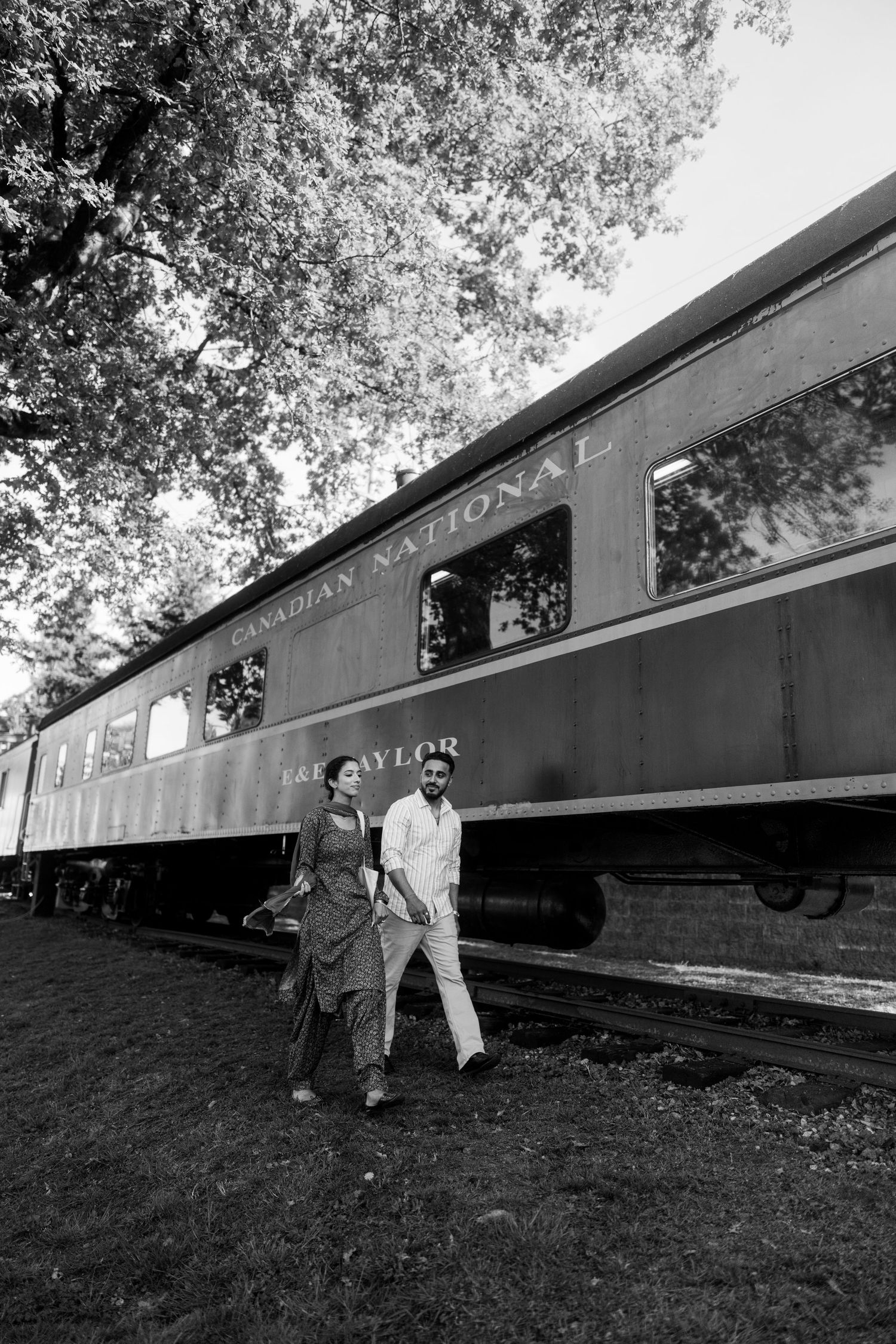 A series of black and white photographs showing two people posing alongside vintage railway cars on a grassy slope.