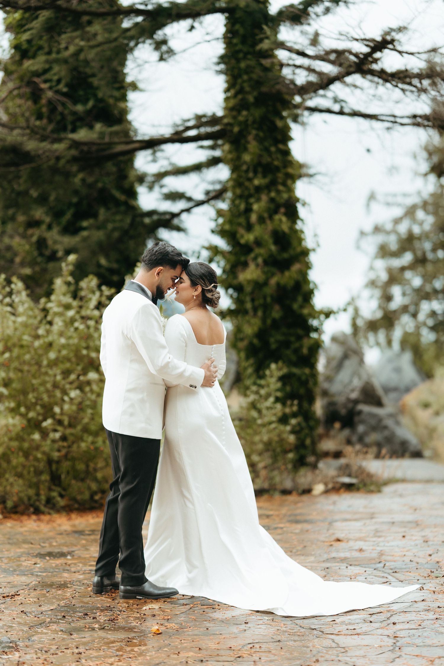 A romantic outdoor wedding moment captured in a series of photos showing a couple embracing on a stone path surrounded by evergreens.