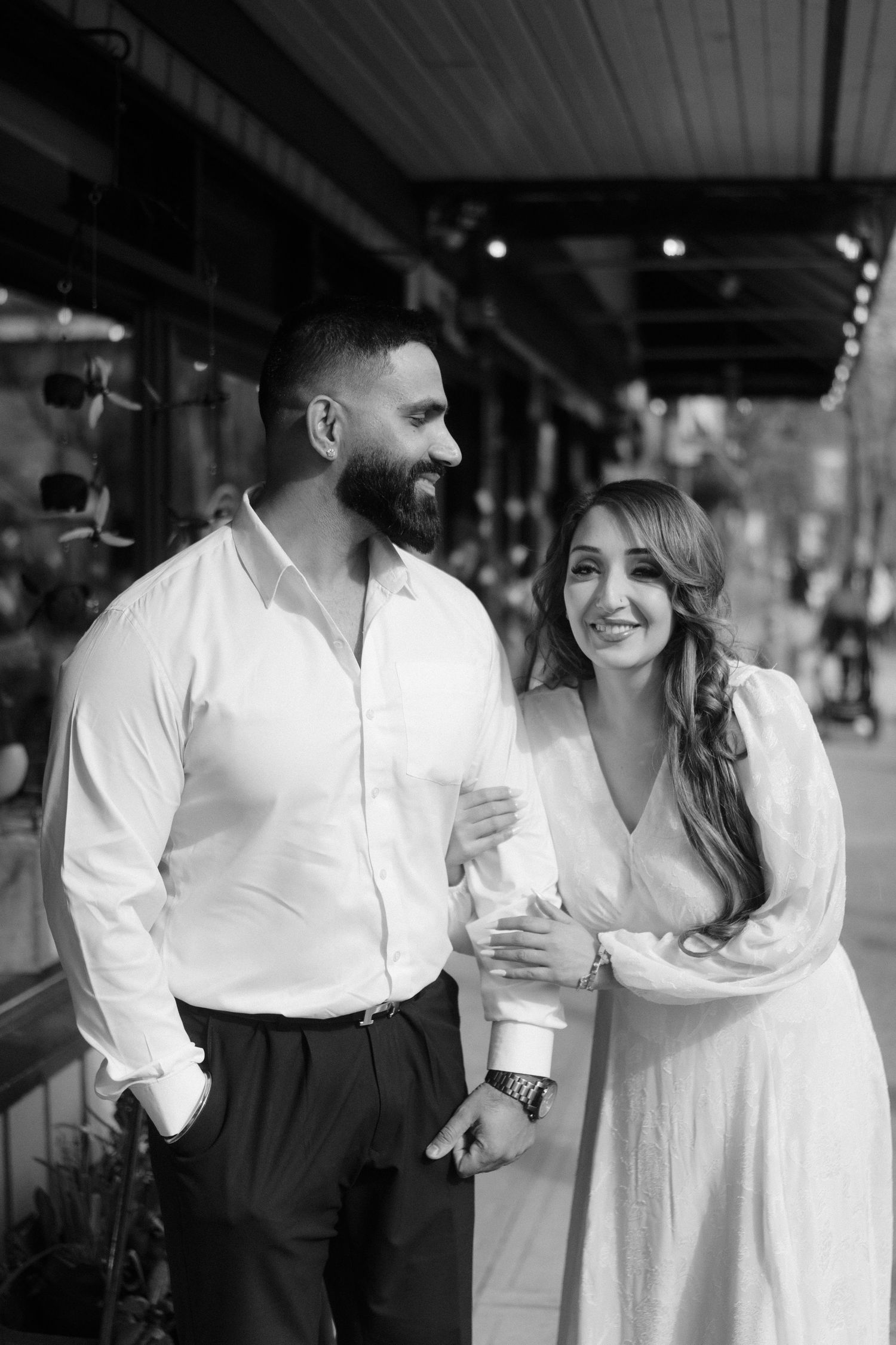 A black and white photo of a couple in formal attire standing under a covered storefront.