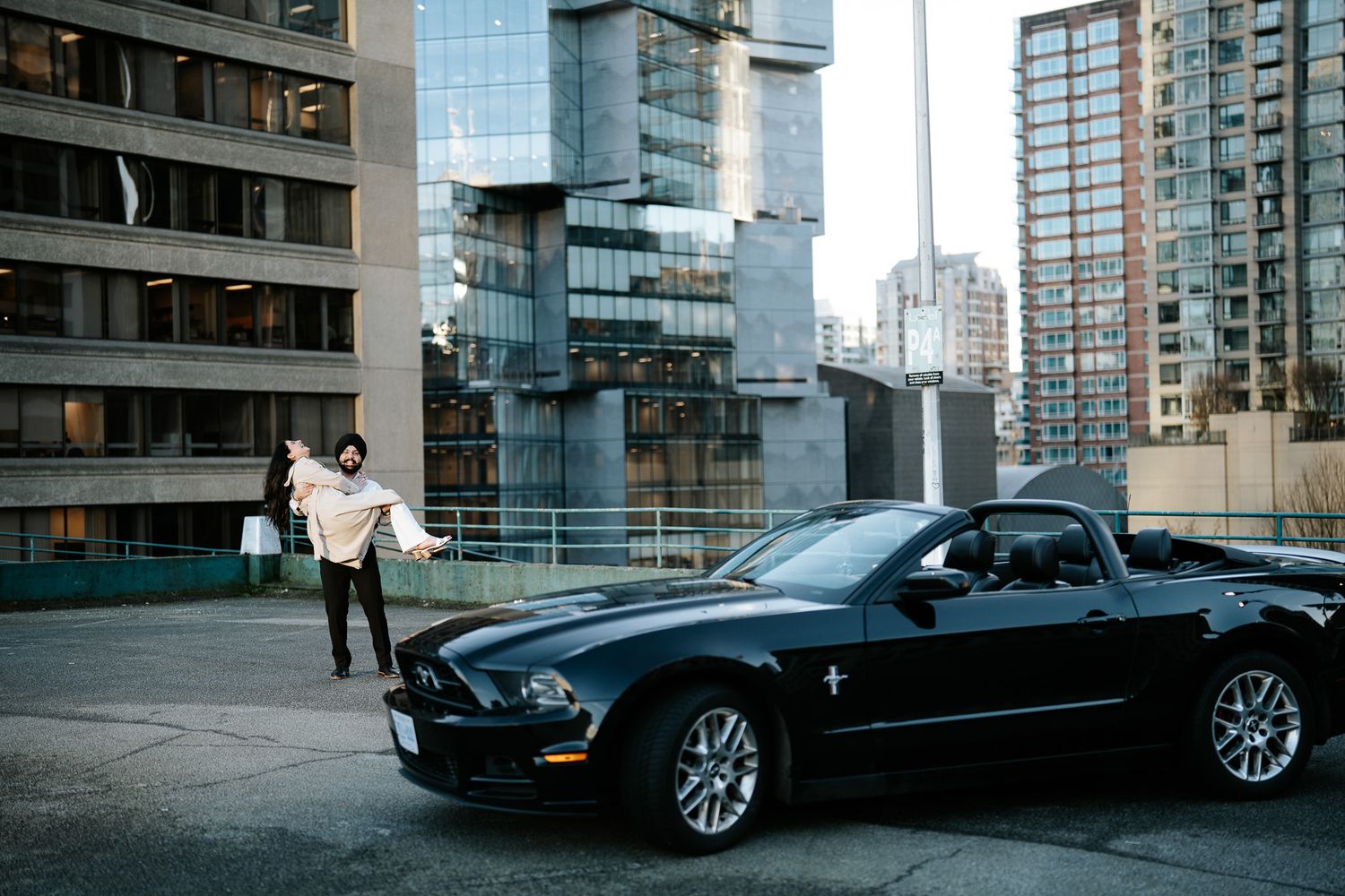 A black luxury car parked on an urban street with modern glass buildings in the background.