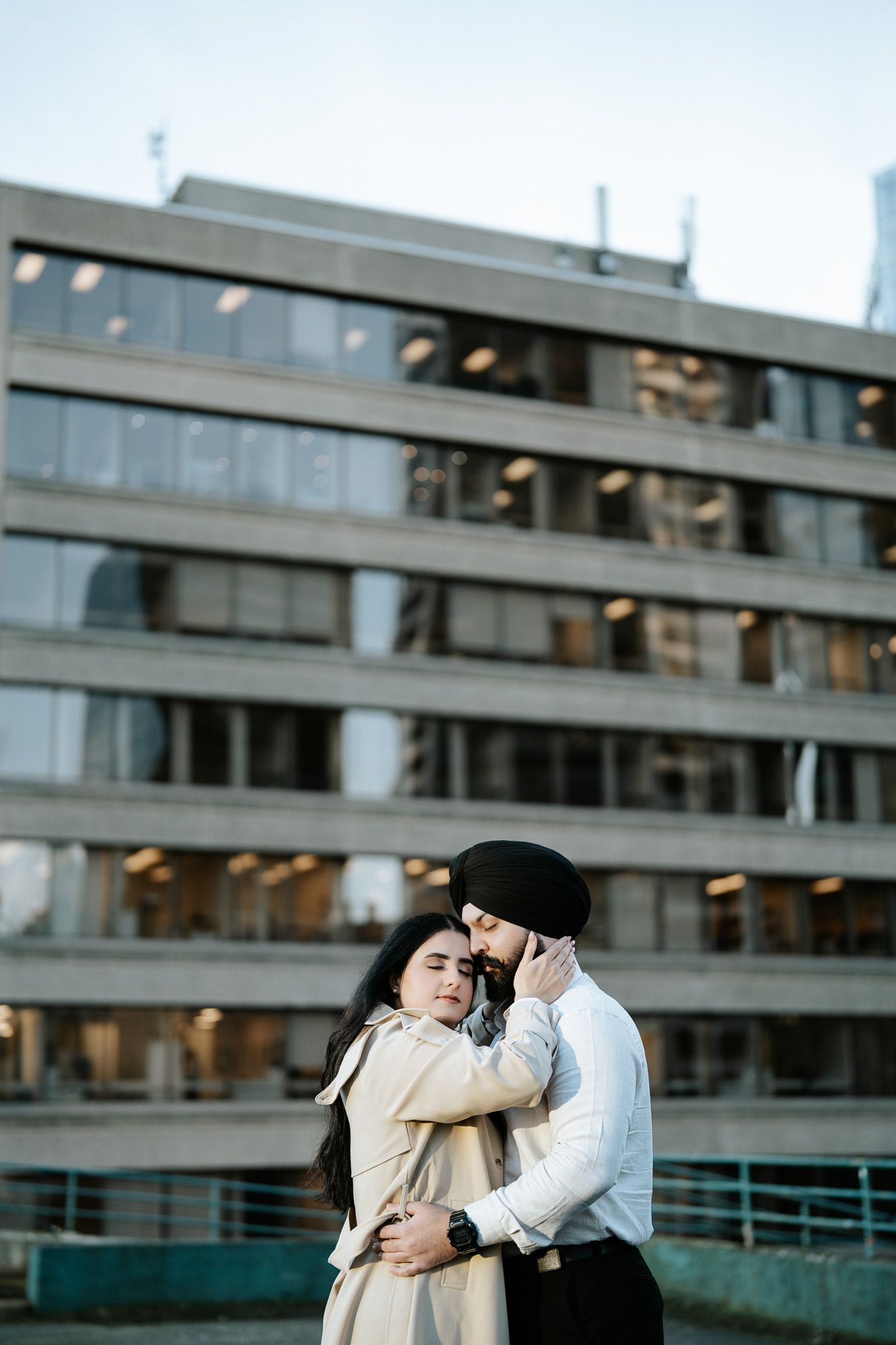 A couple shares an intimate embrace on a rooftop terrace with modern architecture in the background.
