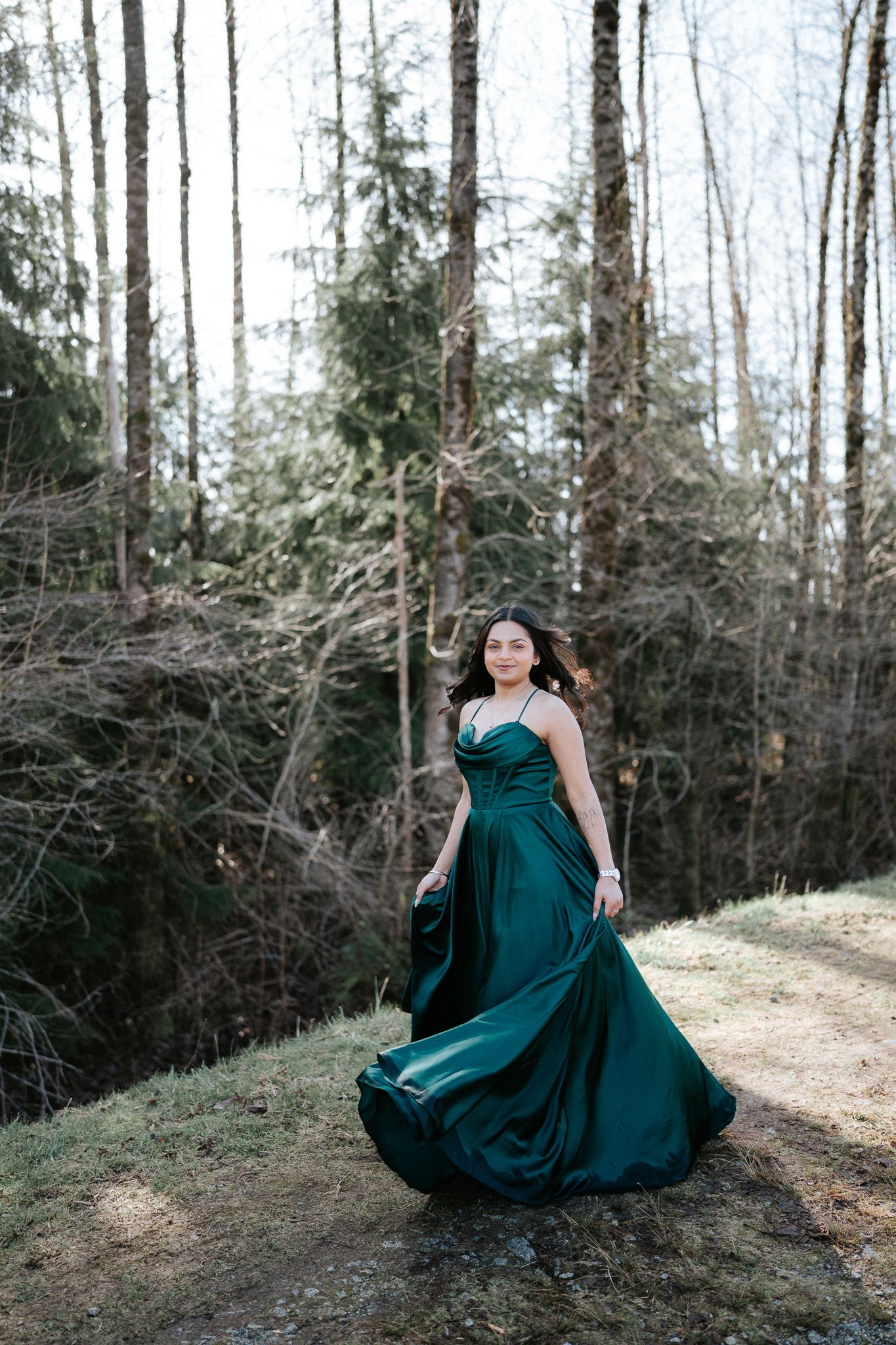 A figure in an emerald green flowing dress poses dramatically on a forest path in a series of artistic shots.