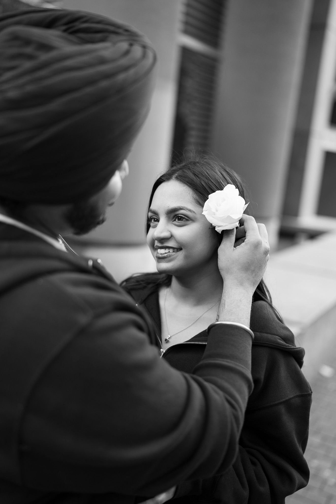 A black and white sequence of images showing someone adjusting a white flower in another person's hair.