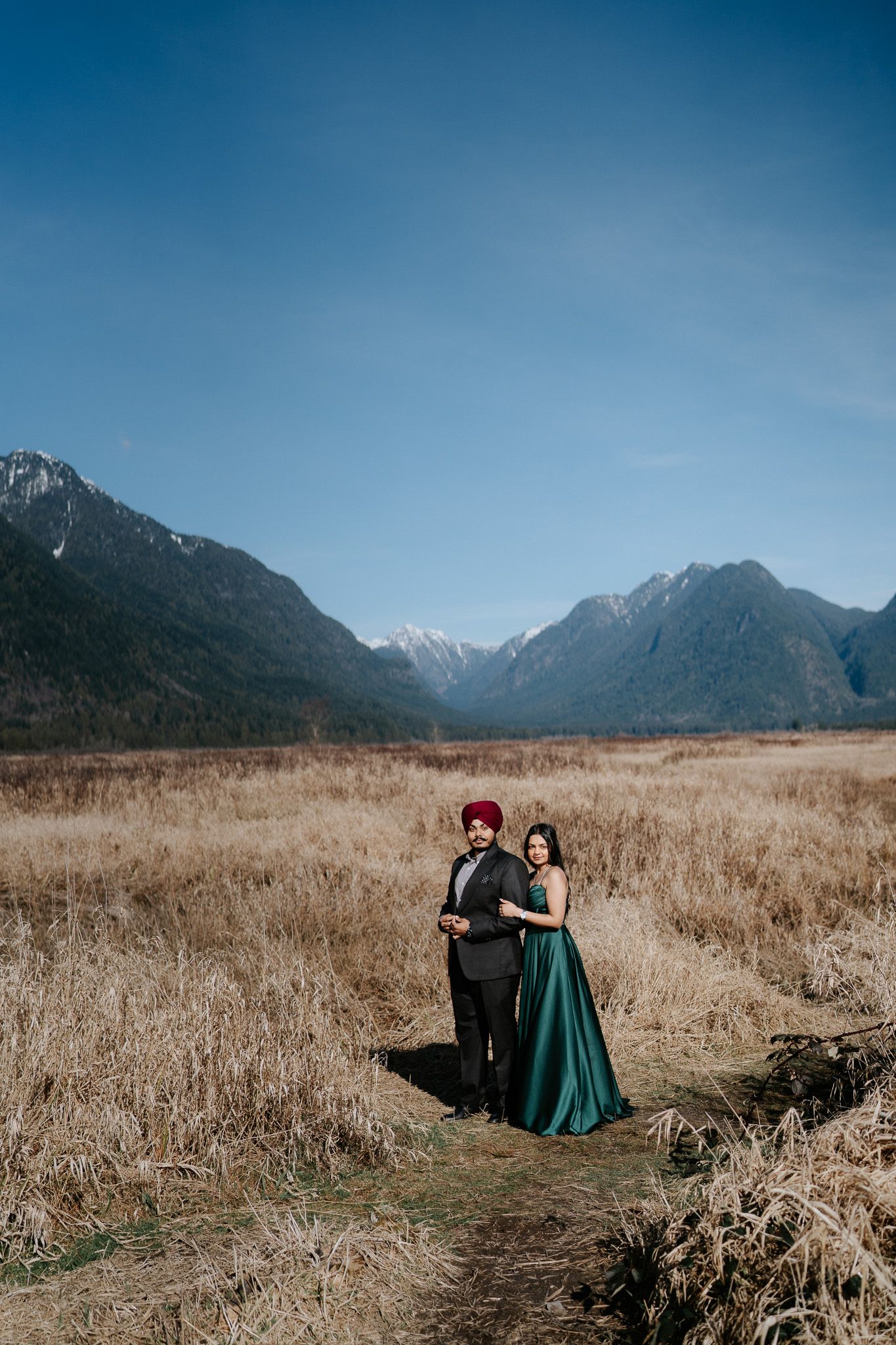A dramatic mountain landscape with snow-capped peaks serves as backdrop to a grassy meadow field.
