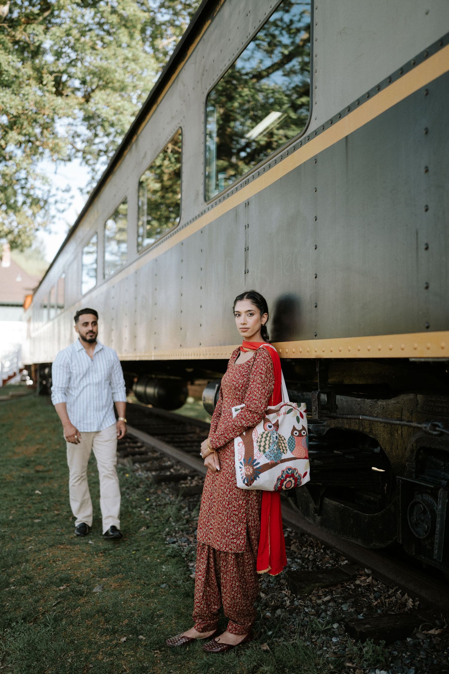 A couple in traditional South Asian attire poses for romantic engagement photos against a rustic train car backdrop.