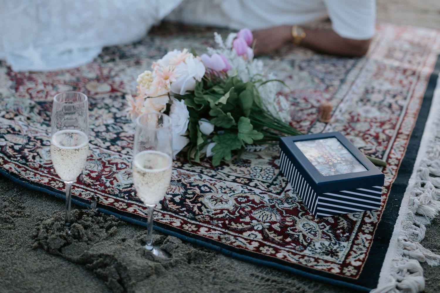 A collection of vintage-style rugs laid out on the ground with glassware and decorative elements at an outdoor event.