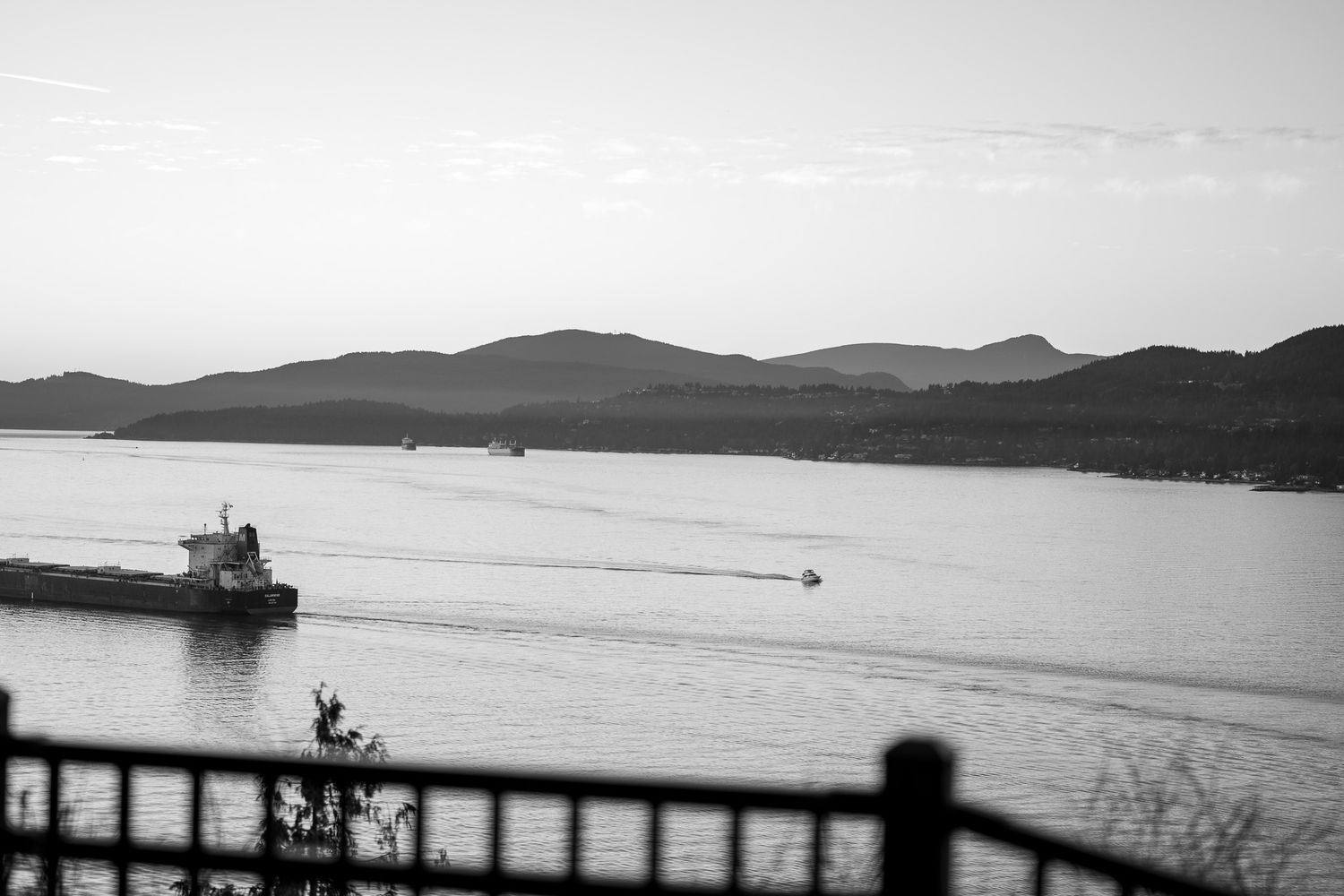 A black and white panoramic view of a mountainous coastline with boats dotting the calm waters.