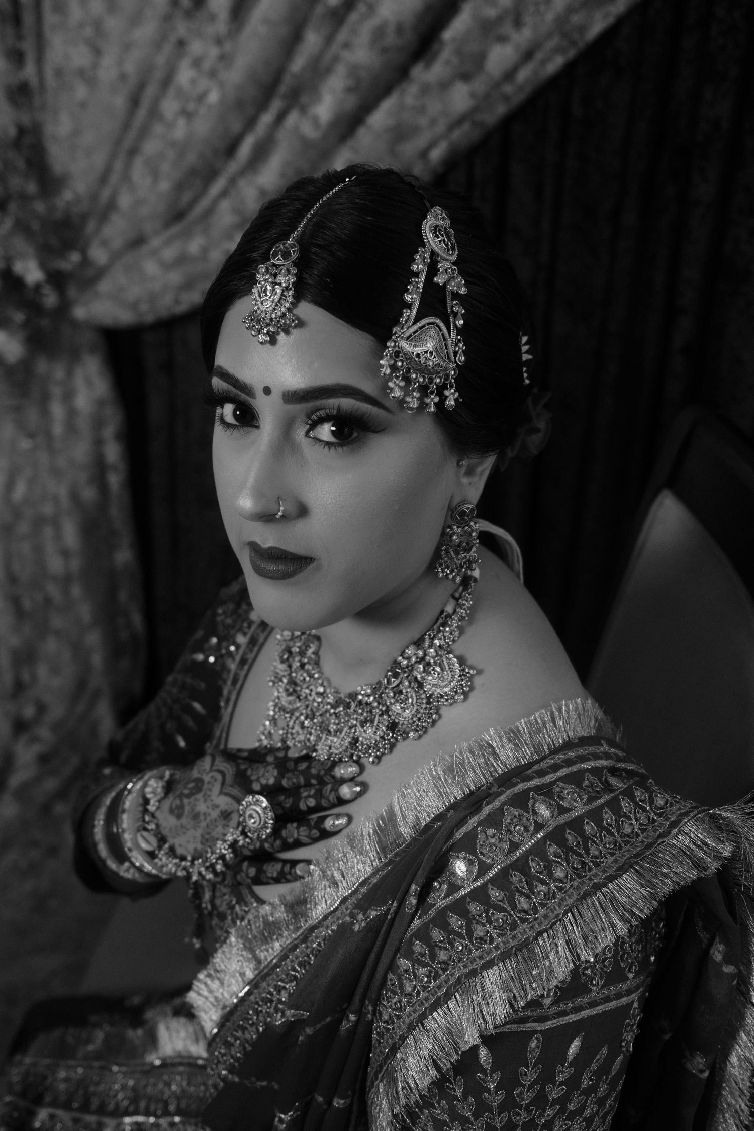 Black and white portrait of a bride in traditional Indian attire with ornate jewelry and mehndi.