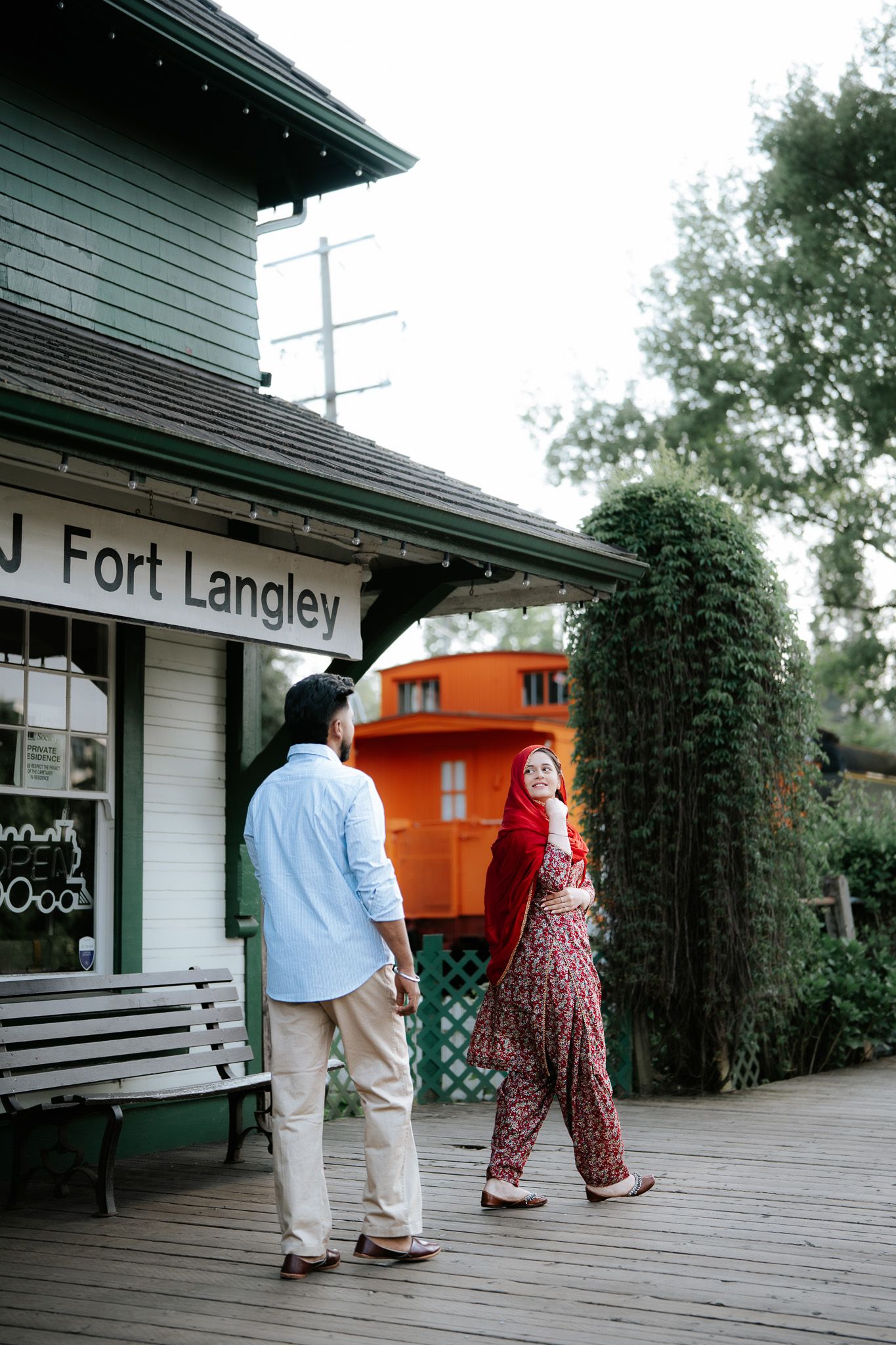 Couple holding hands and walking near the historic Fort Langley train station with orange caboose in background.