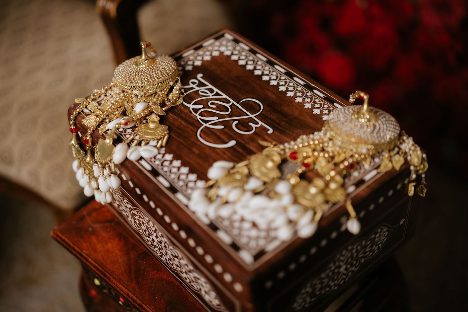 Ornate wooden jewelry box with white inlay designs, adorned with gold Indian bridal jewelry and pearl accessories.
