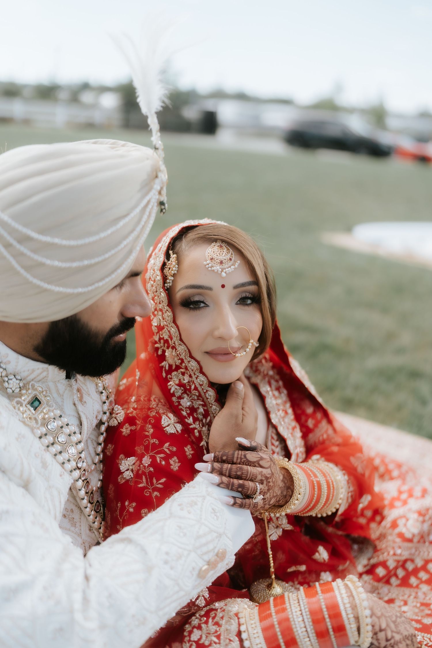 Sikh bride in red lehenga and groom in white sherwani sharing a tender moment during their traditional Indian wedding ceremony.
