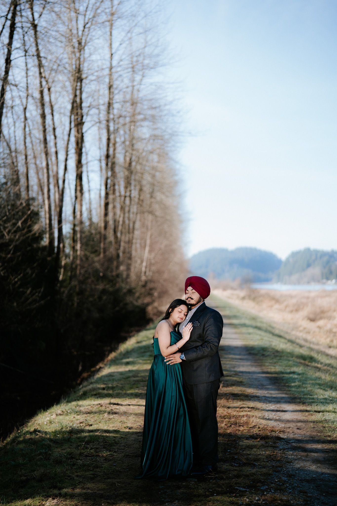 A romantic couple embraces on a misty tree-lined path during a winter engagement photo session.
