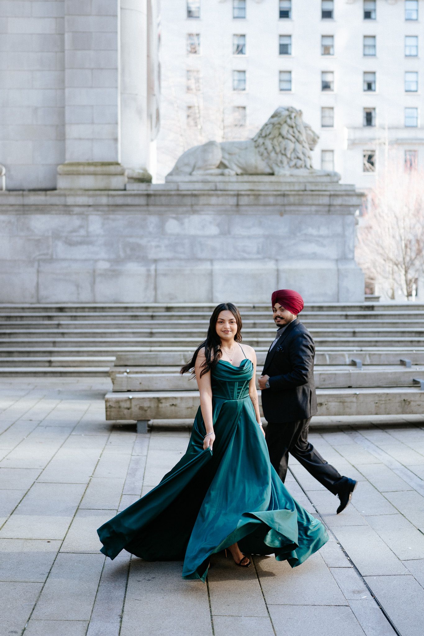 A couple shares a romantic moment on marble steps, with her emerald dress flowing elegantly in motion.
