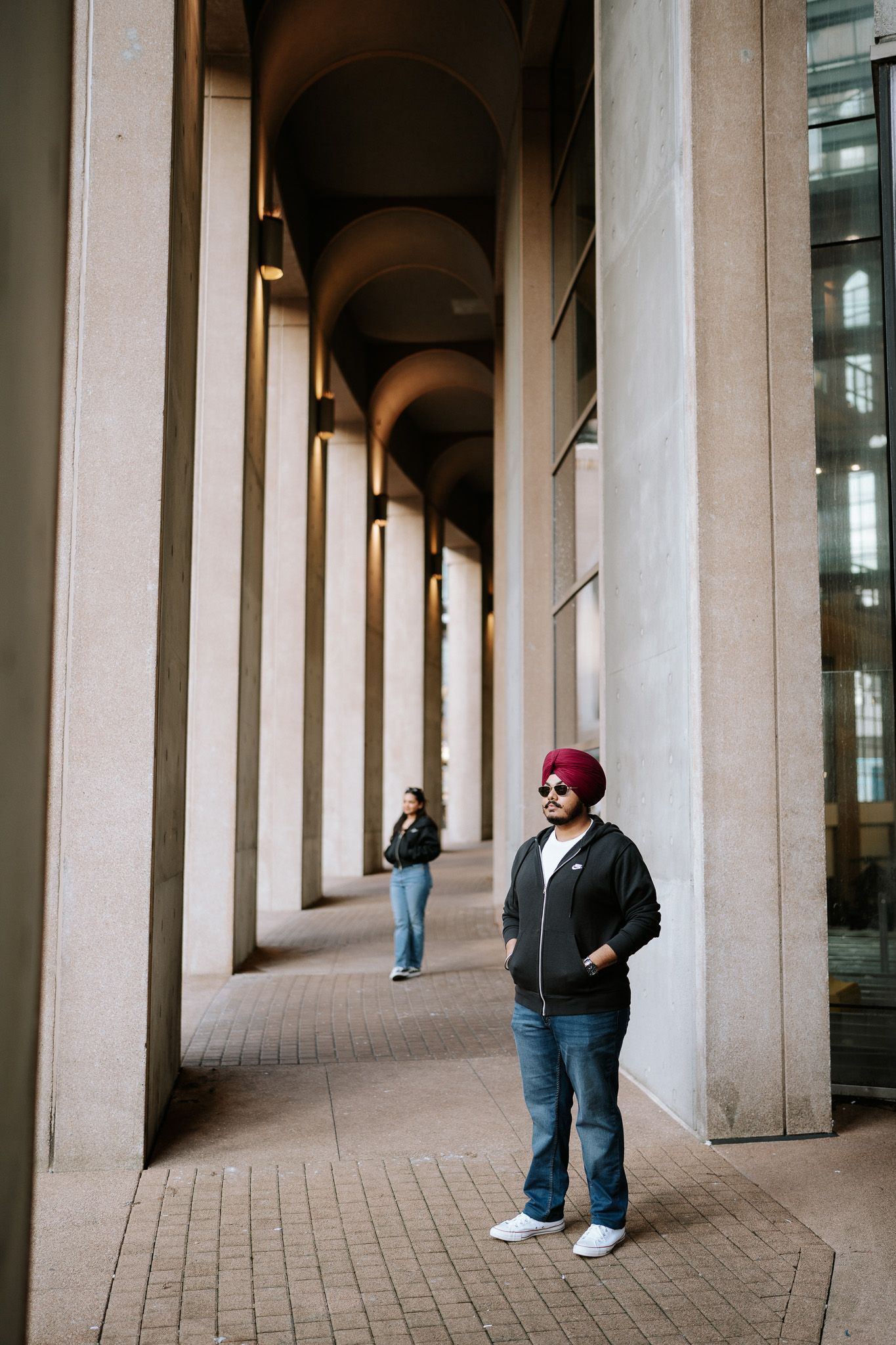 Person wearing a red turban stands in a colonnade hallway with repeating stone archways and columns.