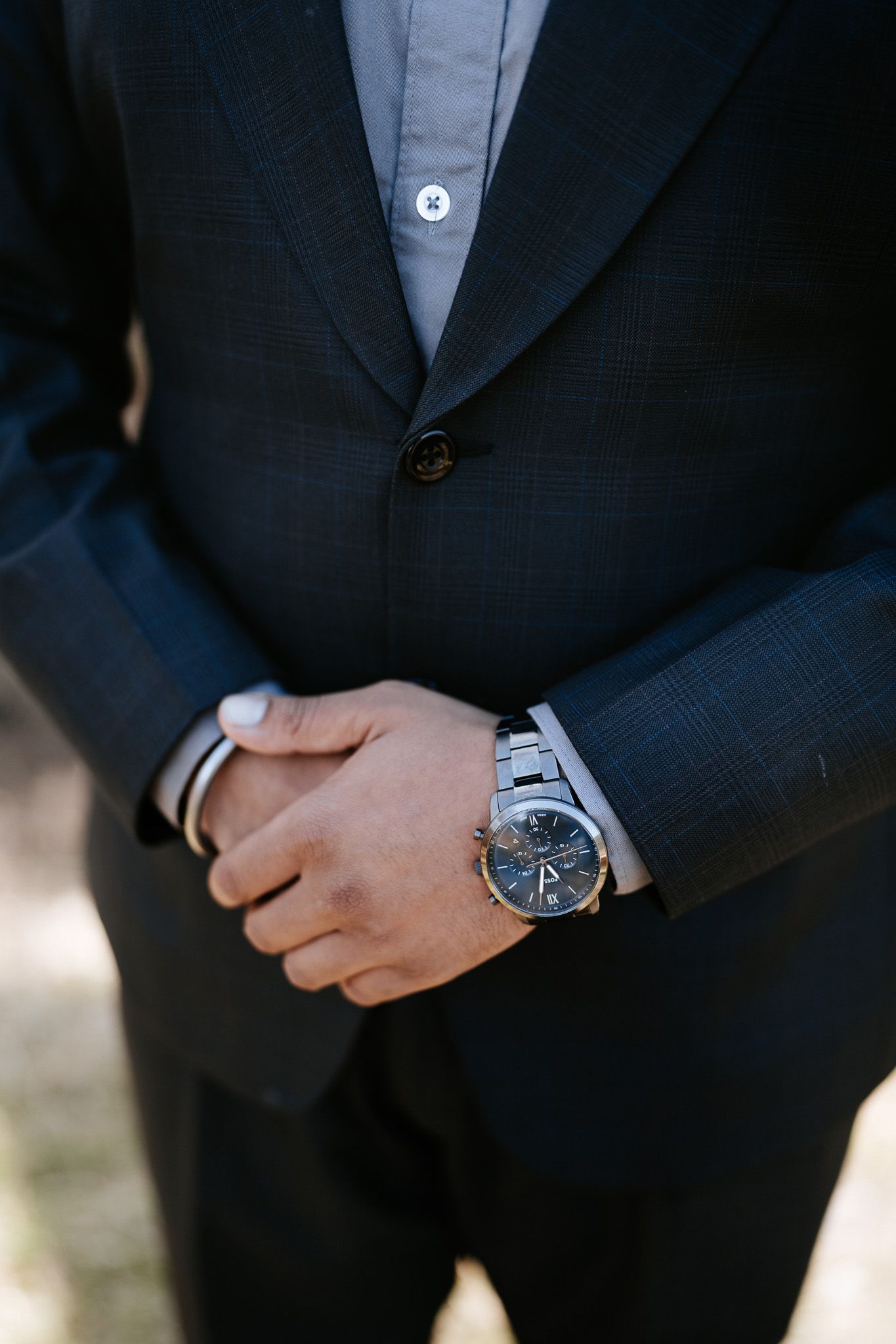 Close-up view of a navy blue suit jacket sleeve with a silver watch visible on the wrist.