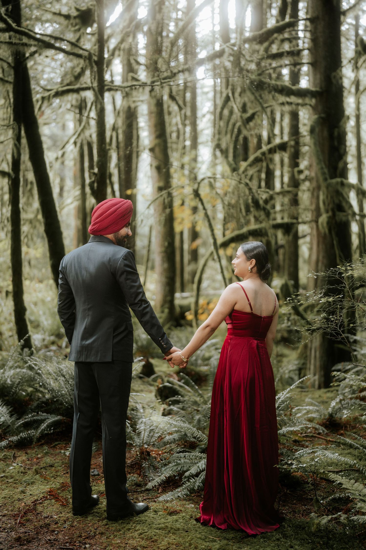 Couple in formal wear exploring a lush forest floor covered in ferns.