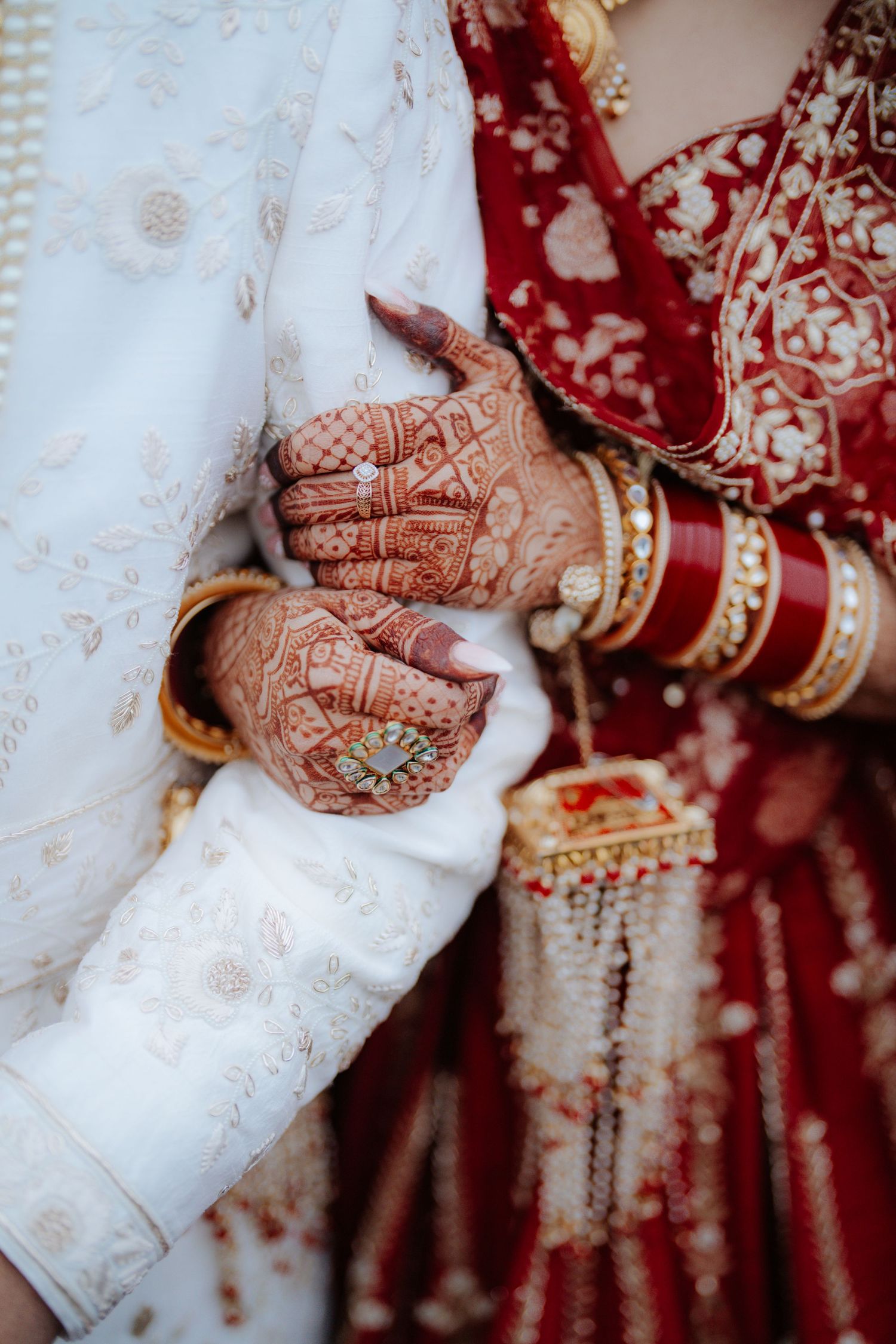 Detail shot of hands with intricate henna designs and traditional Indian wedding bangles.