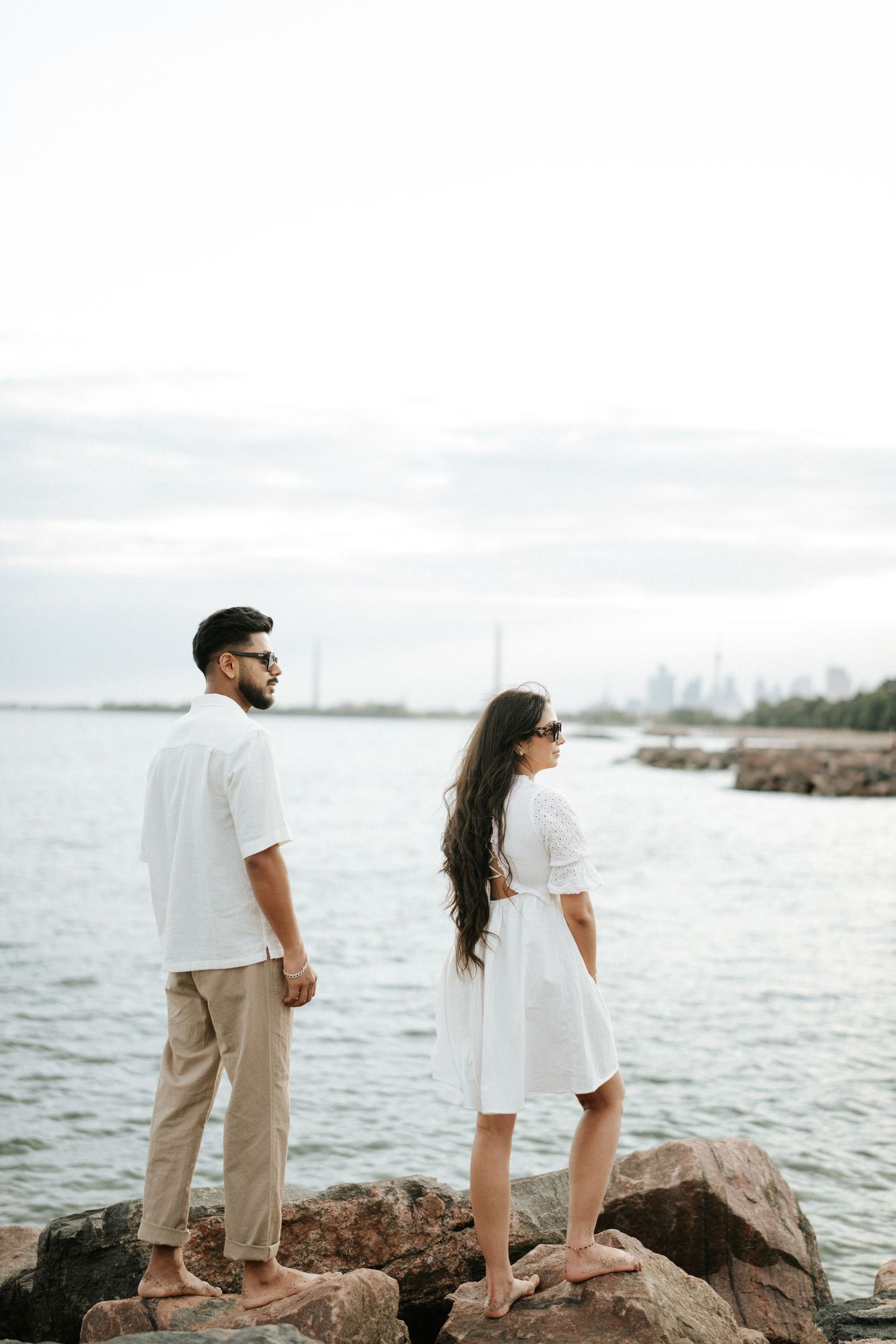 Couple standing on coastal rocks overlooking the ocean at sunset.