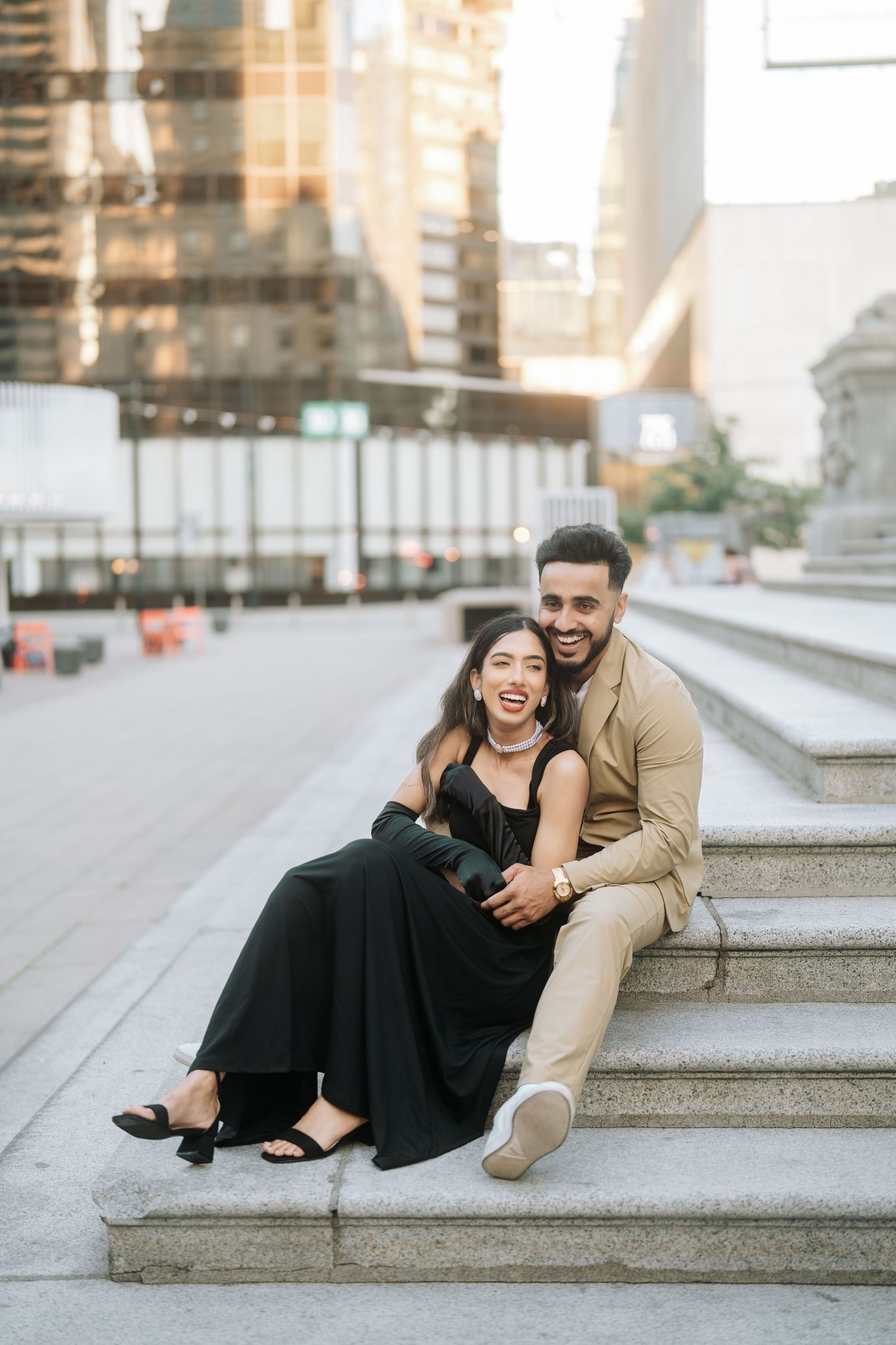 Happy couple sitting and laughing together on outdoor stone steps in an urban setting during golden hour.
