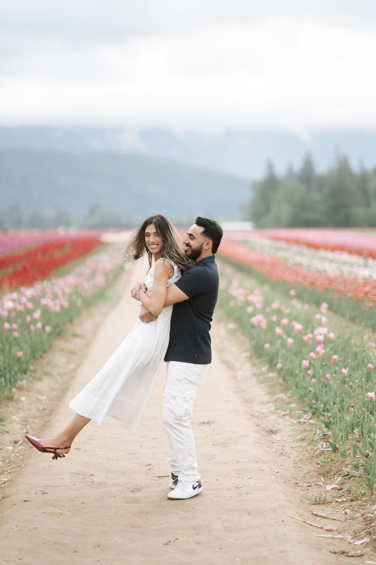 A couple dances playfully in a blooming tulip field on a misty spring day.