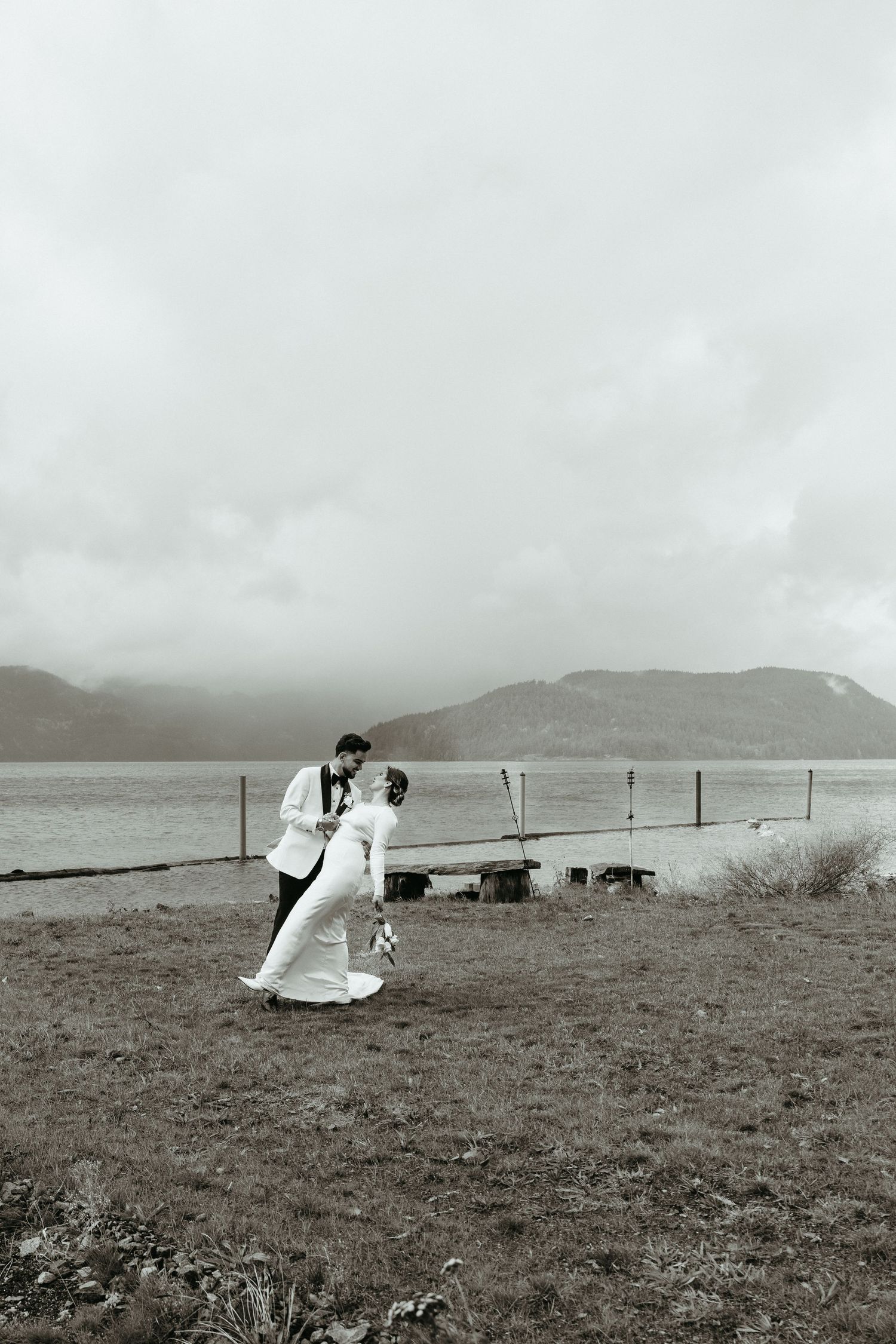 Black and white photos show a couple in wedding attire embracing on a windswept coastal hillside with mountains in background.