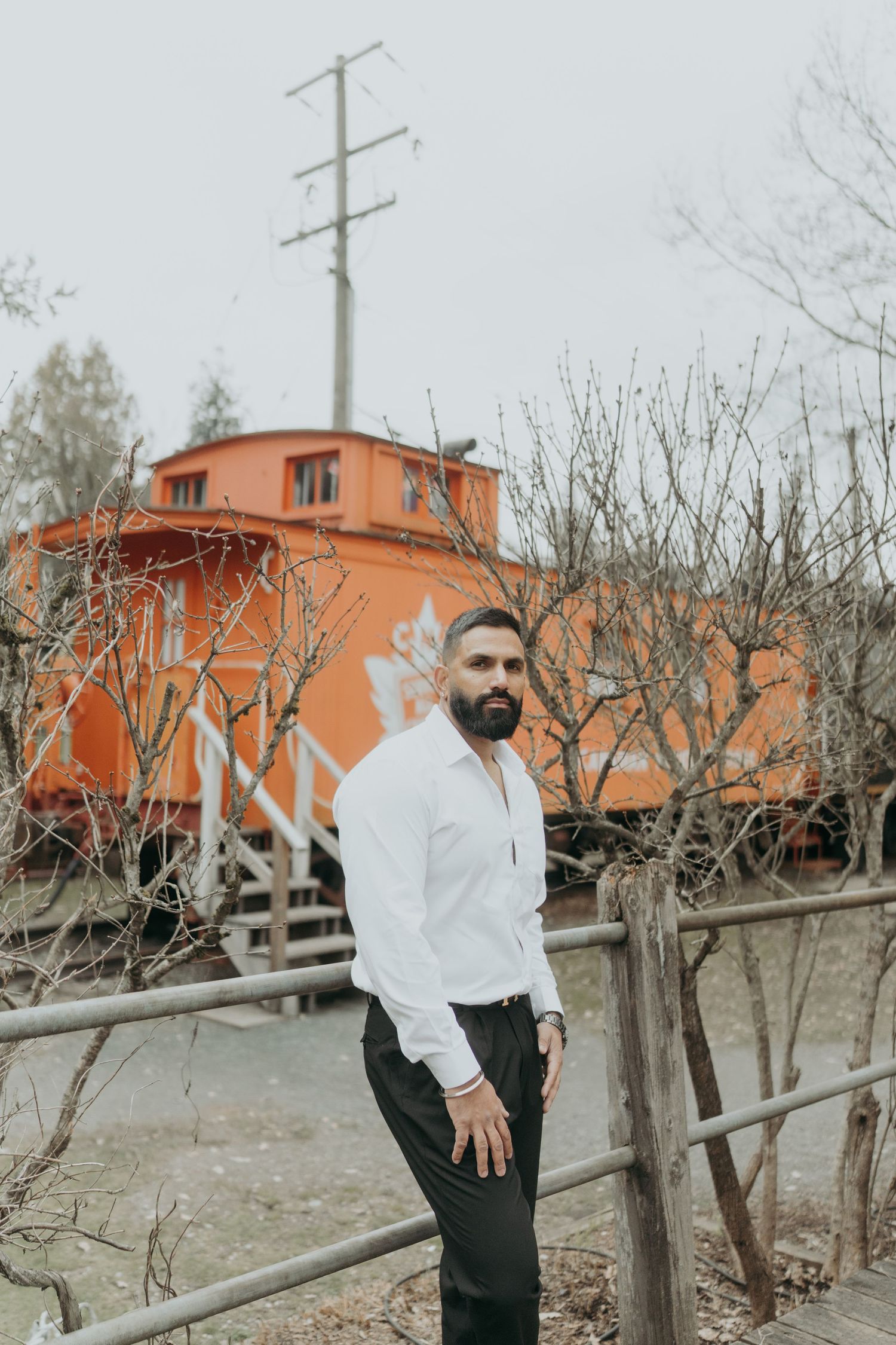 Stylish portrait session near vintage orange train car with rustic wooden fence.