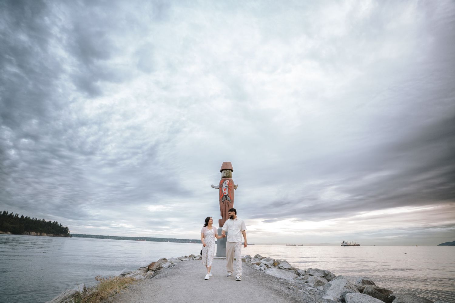 Two people in white clothing pose together against a dramatic coastal landscape.