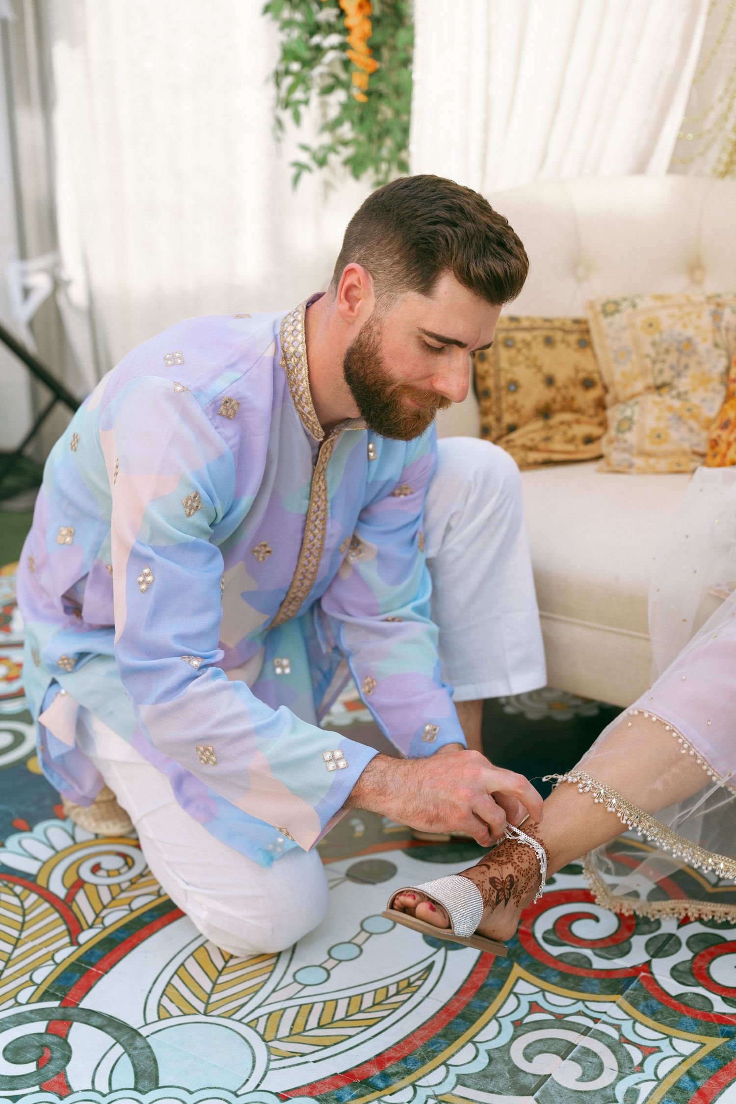 Groom in pastel kurta placing wedding ring on bride's henna-adorned hand during South Asian ceremony.
