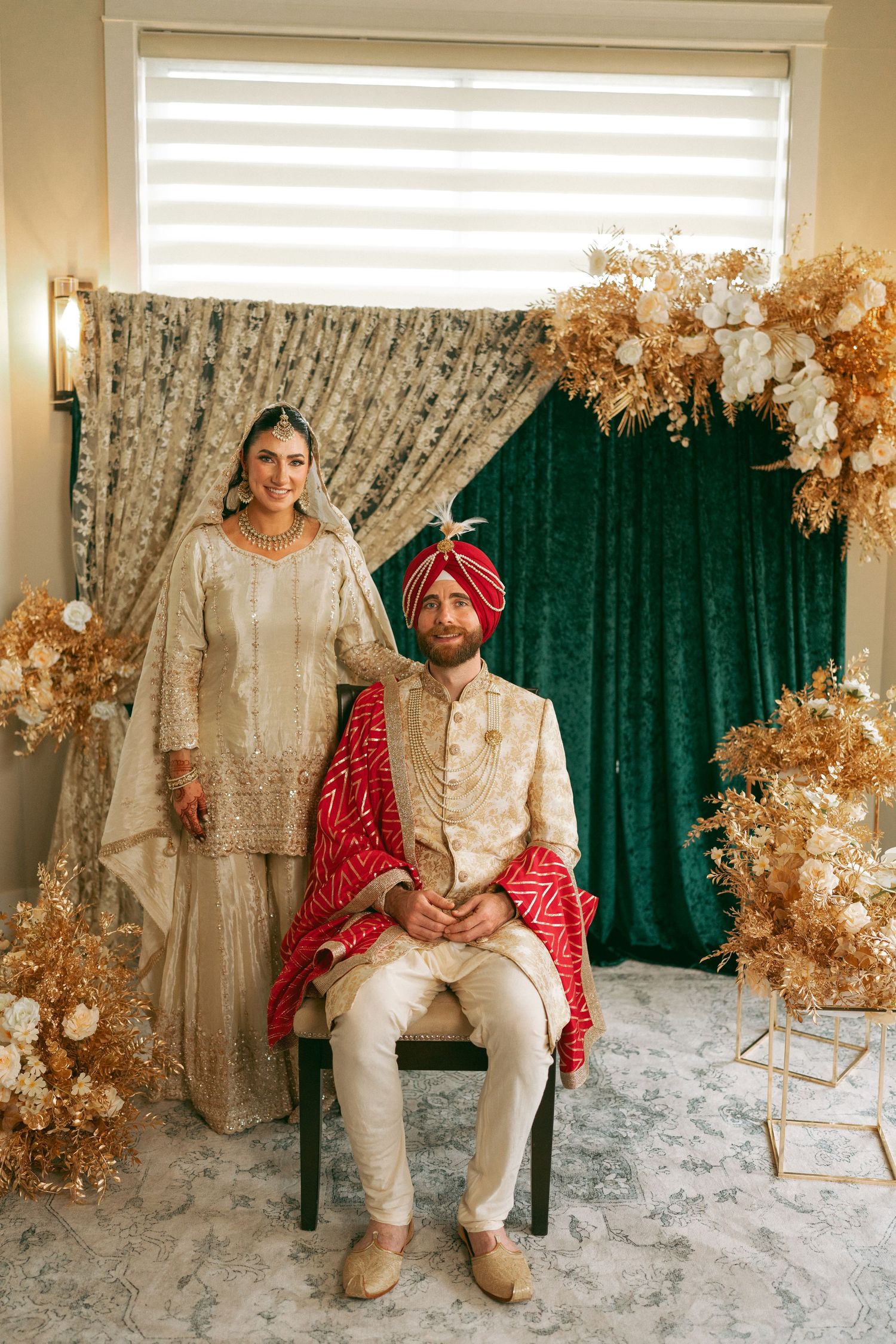 Sikh couple in traditional wedding attire, bride in gold salwar kameez, groom in cream sherwani and red turban.