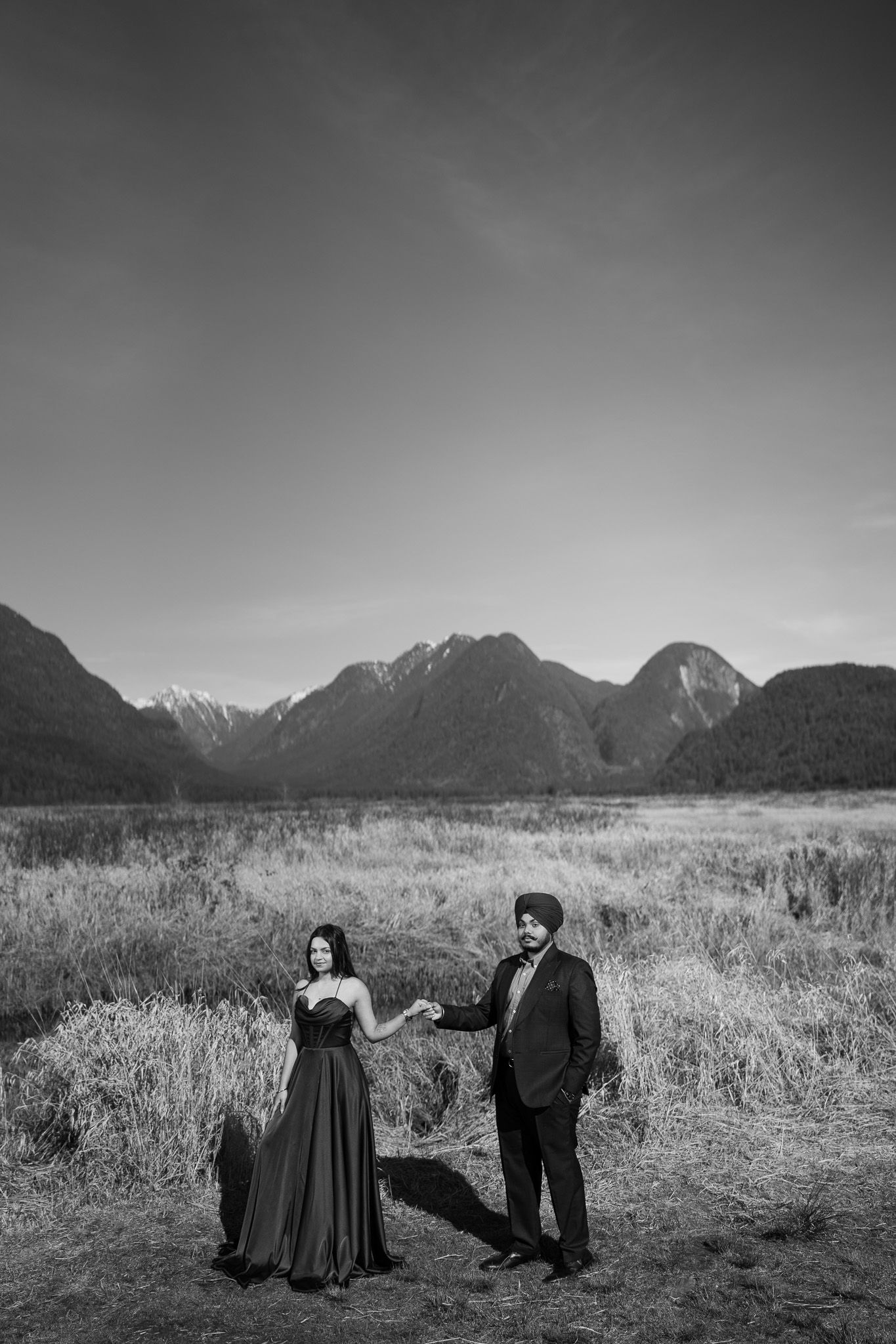 A black and white panoramic series of a couple walking through a mountain meadow with dramatic peaks in the background.