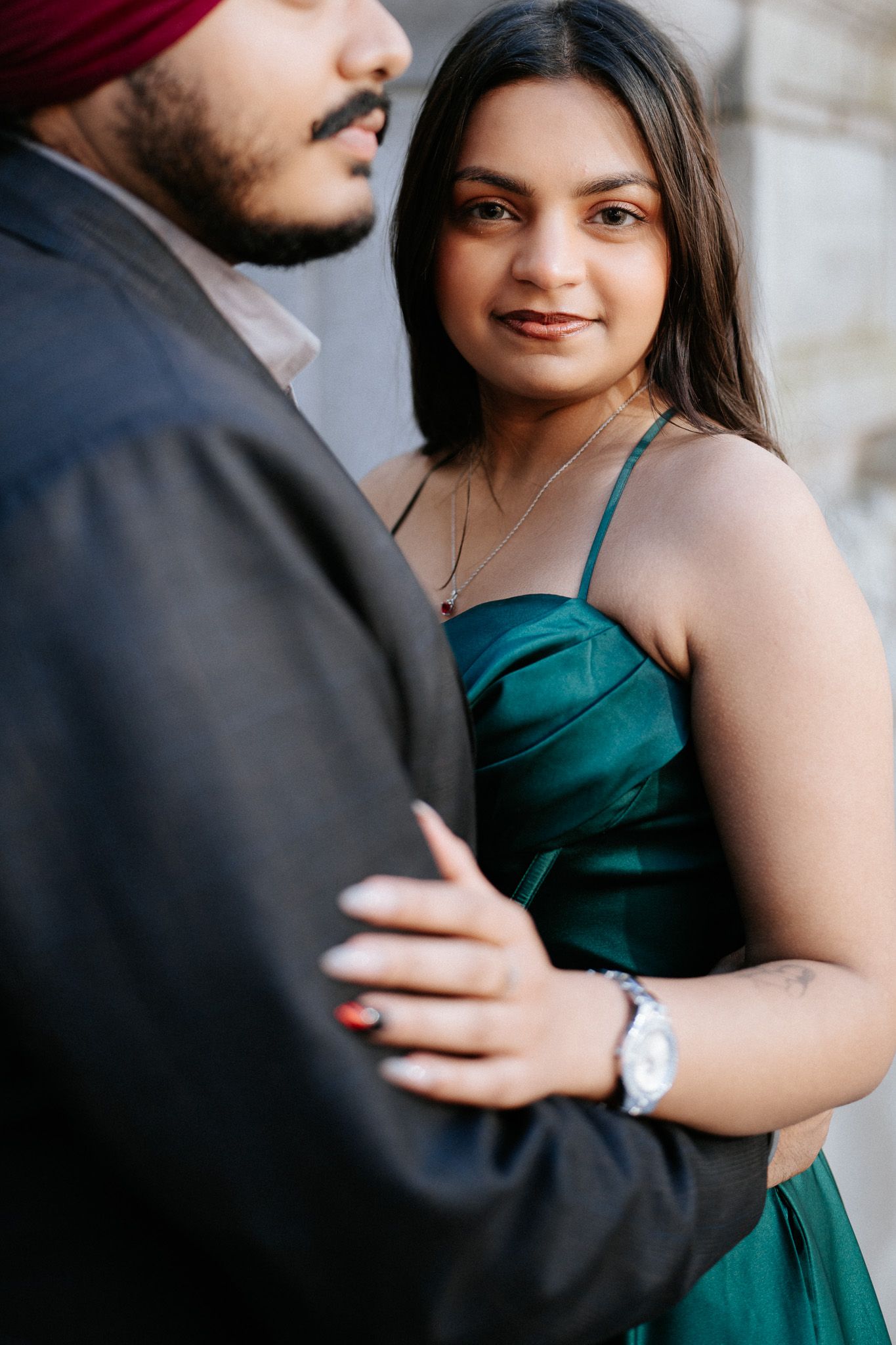 A romantic couple in formal attire embraces, with her wearing an elegant emerald green dress and him in a dark suit.