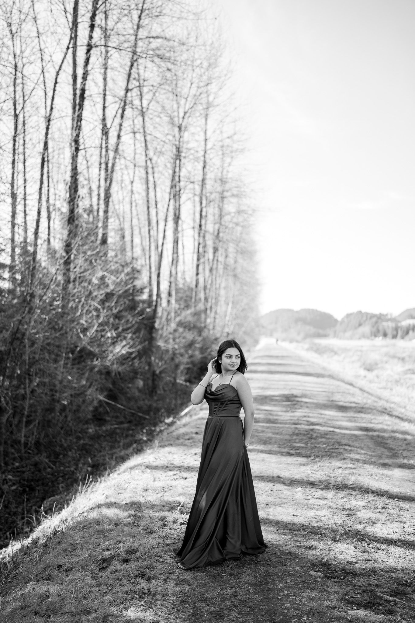 A figure in a flowing black dress stands alone on a misty forest path in a dramatic black and white composition.