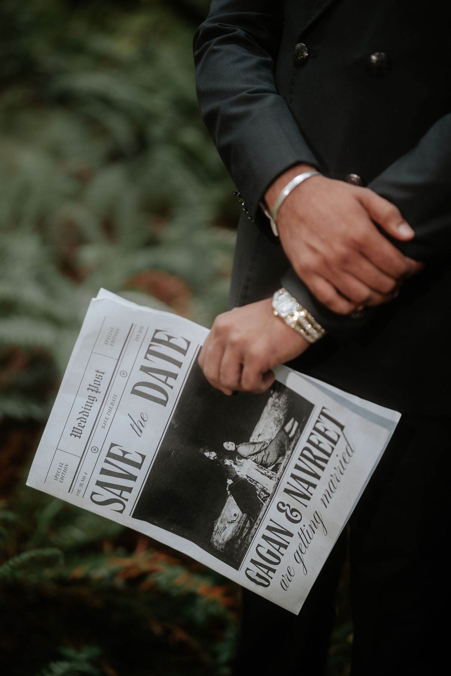 Close-up of hands holding a save-the-date newspaper announcement with jewelry details.