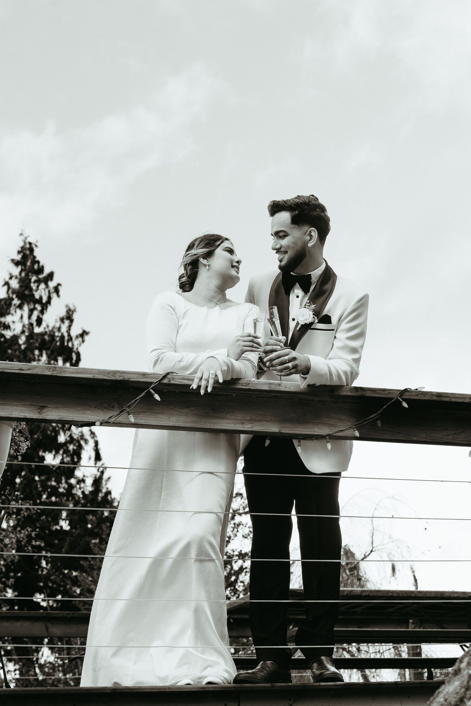 A couple shares a romantic moment while leaning on a wooden railing in a black and white vintage photograph.